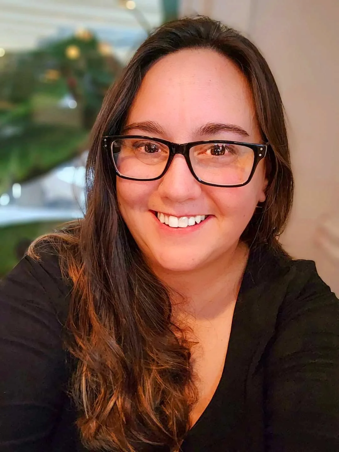 Smiling woman with glasses and long wavy hair in a casual setting.
