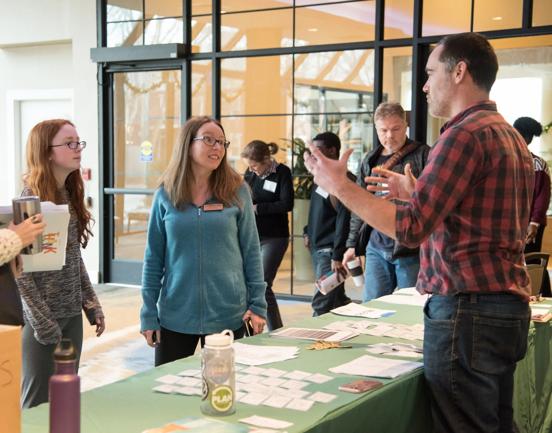 People engaging in a discussion around a table with pamphlets and brochures at an indoor event or conference.