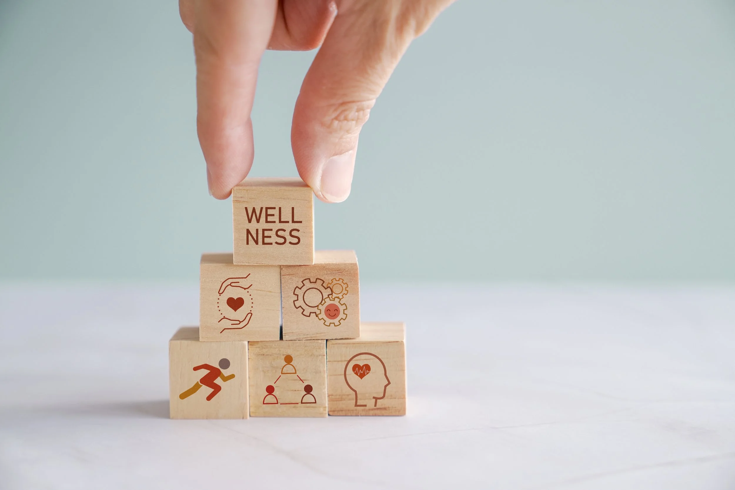 Stacked wooden blocks with health and wellness icons, with the top block labeled "Wellness".