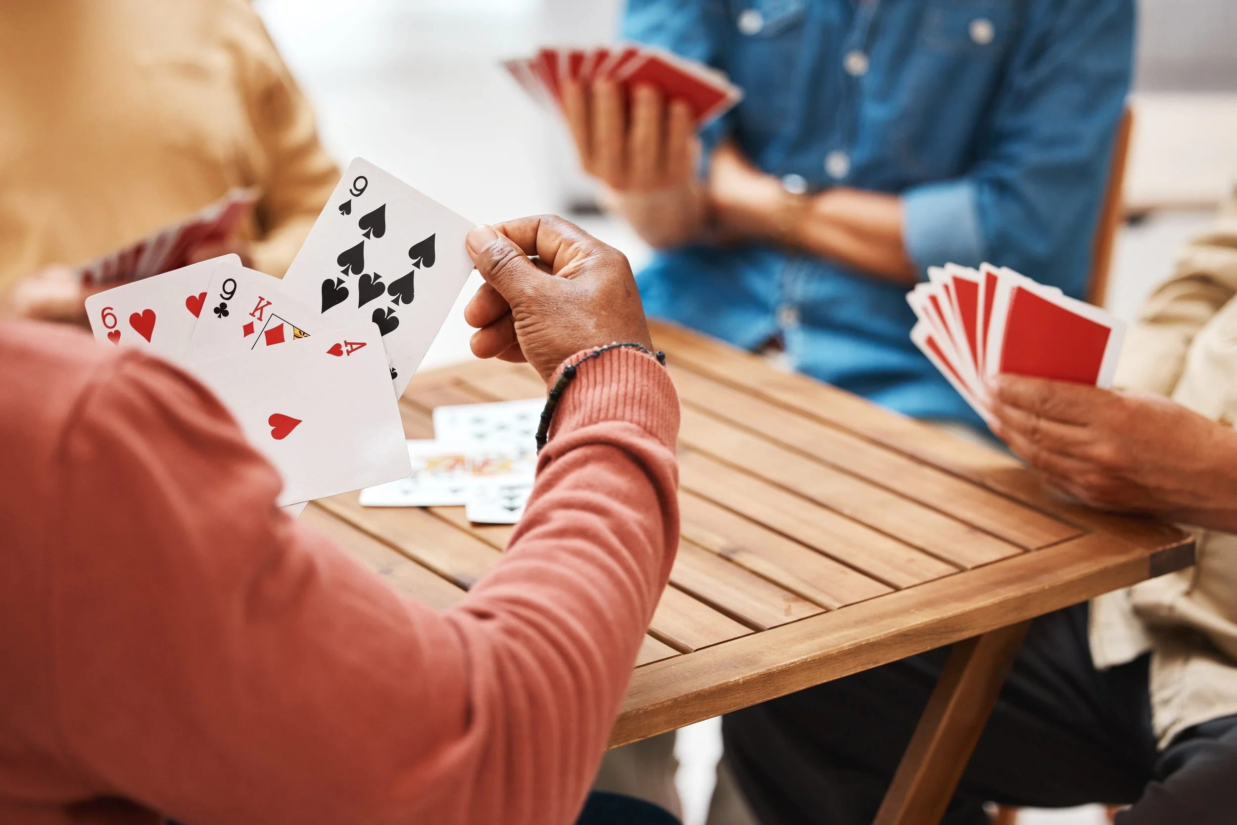 People playing a card game at a wooden table, with various playing cards visible in their hands.