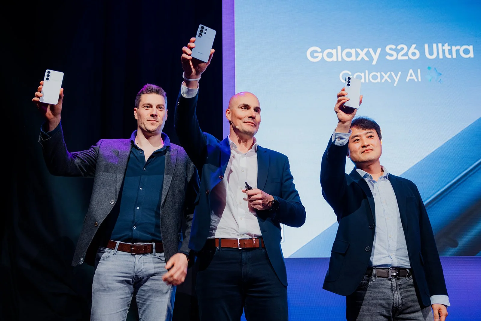B2 Photography Jakob Hallaert  - Drie mannen op een podium, elk houdend een witte smartphone met drie camera's, bij de lancering van de Samsung Galaxy S26 Ultra.