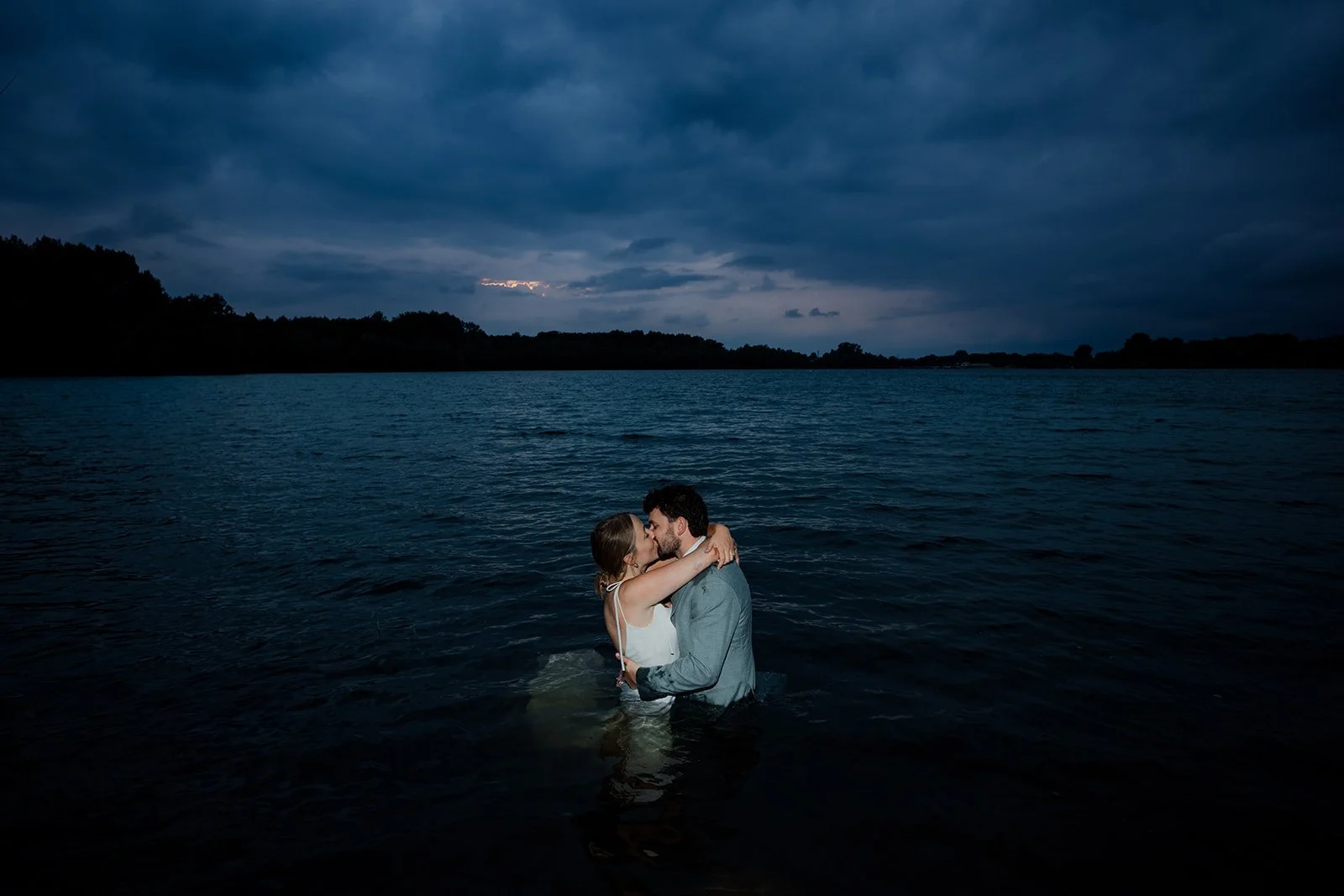 B2 Photography Jakob Hallaert  - Een stel dat in een meer staat en elkaar kust tijdens de schemering onder een donkere, bewolkte hemel.