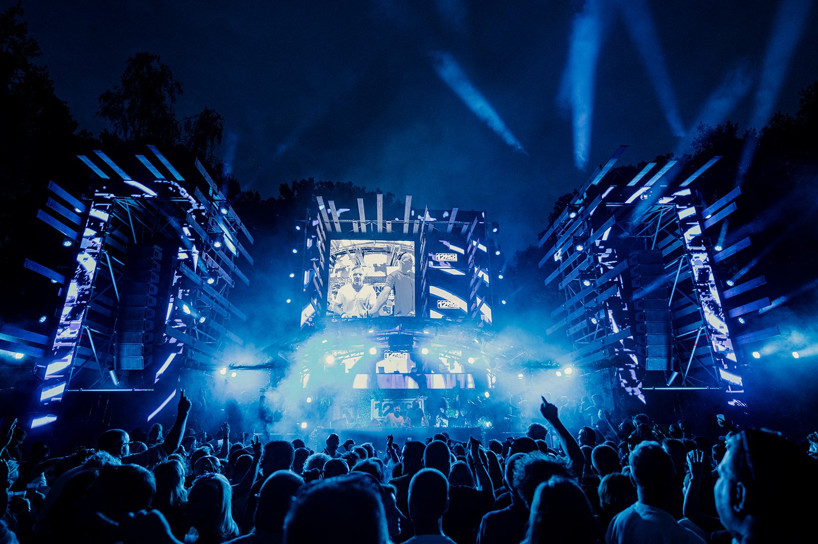 B2 Photography Jakob Hallaert  - een groot muziekfestival met een live optreden onder een donkerblauwe hemel, omringd door verlichte podiumstructuren en een publiek dat danst en naar het stage kijkt.