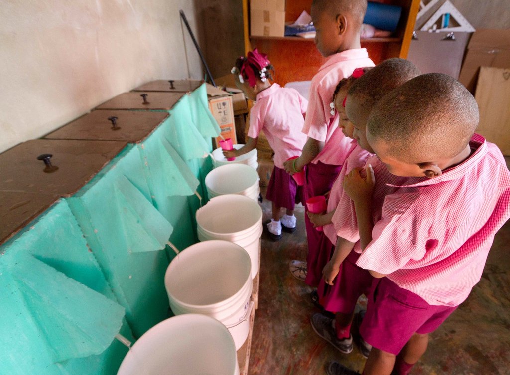 School children in Haiti fill cups of safe water.