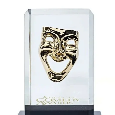 A glass award featuring a gold comedy mask with a smiling face, with the text 'American Academy of Achievement Awards' at the base. American Comedy Award for Judy Gold.