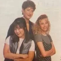 A woman, comedian Judy Gold, standing behind two young girls, one of which is Margaret Cho, smiling for a photo.