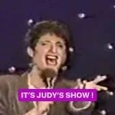 Screenshot of Judy's show with her singing passionately and a purple caption saying 'IT'S JUDY'S SHOW!'