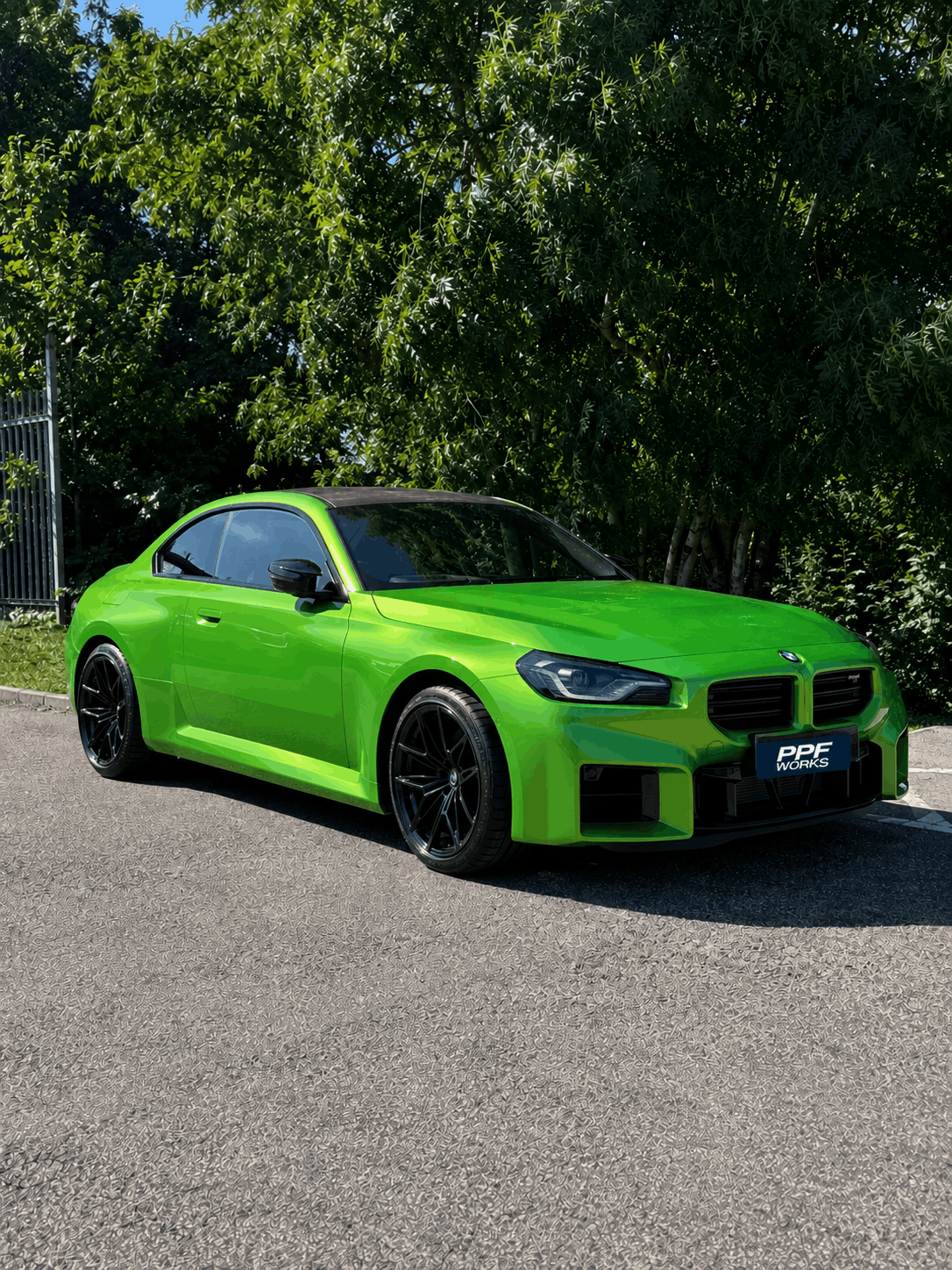 A bright green sports car parked on the side of a paved road, with lush green trees in the background.