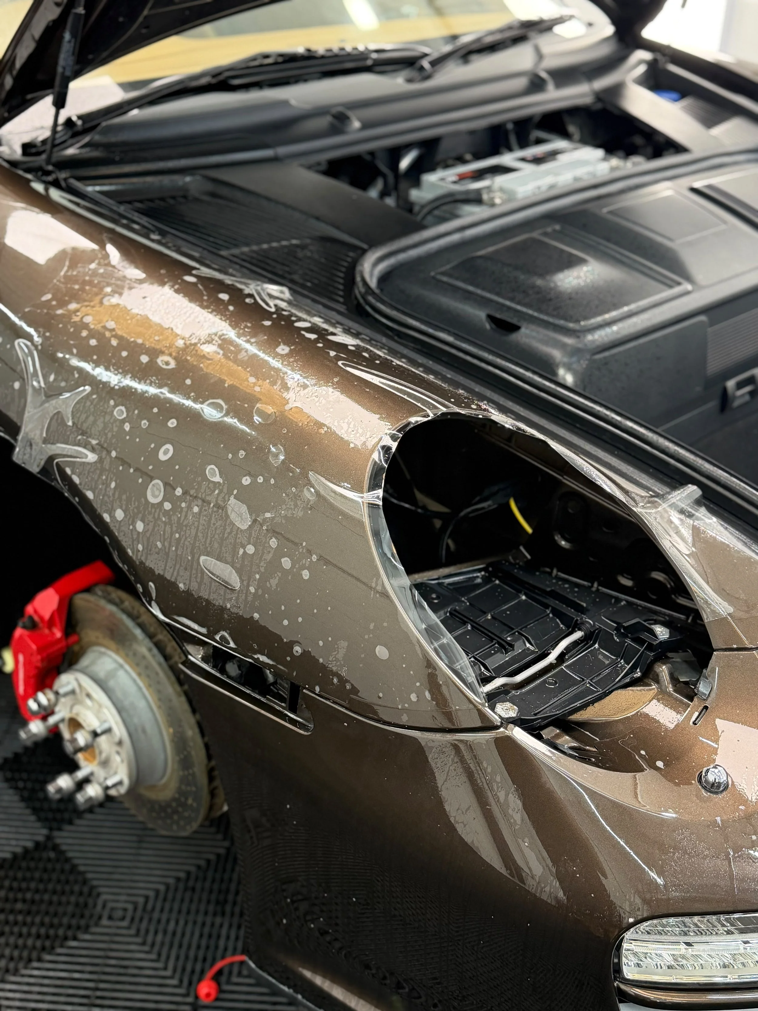 Close-up of a car with the hood open, showing the engine bay and part of the front bumper, with some water droplets on the car's surface.