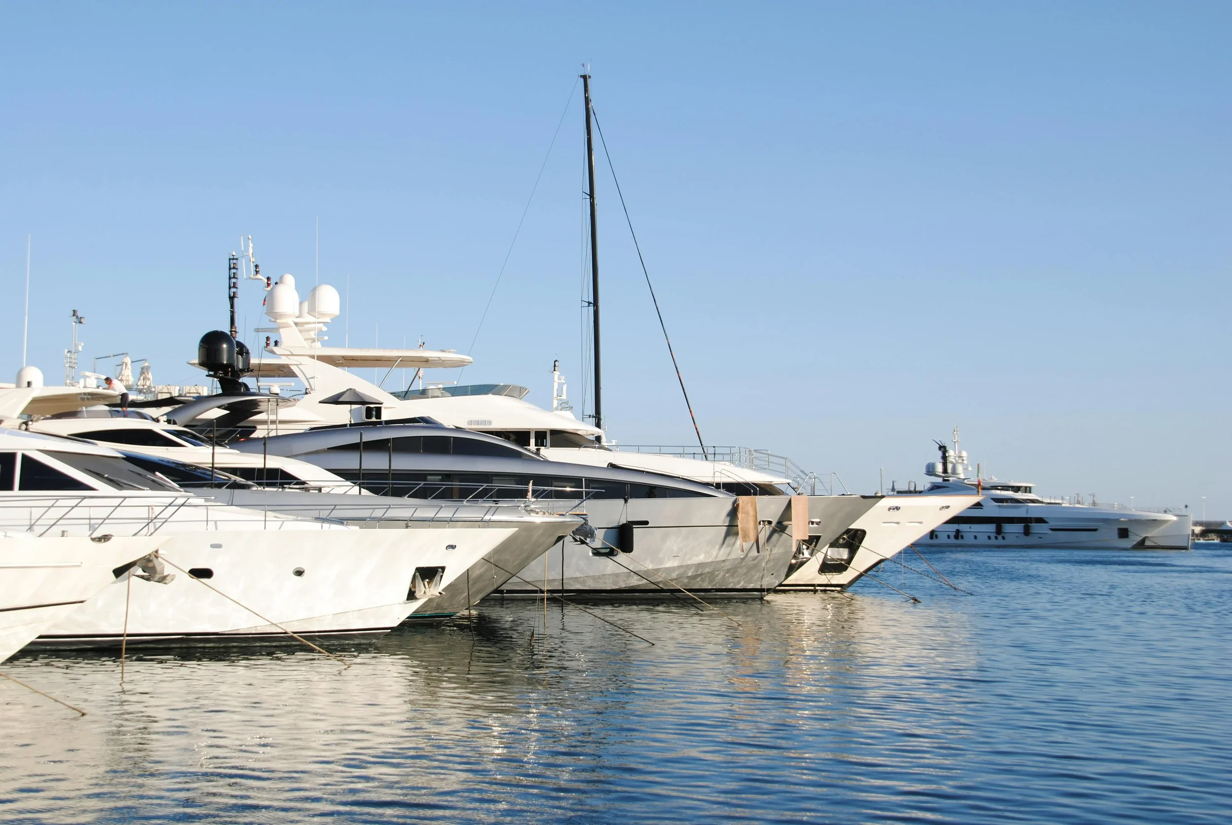 Multiple luxury yachts docked at a marina during daytime with a clear blue sky.