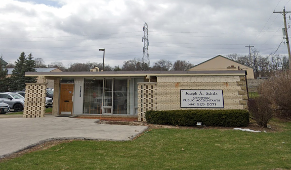 A single-story office building with a sign for Joseph A. Schilz, Certified Public Accountant, on a sunny day with some clouds, with cars parked nearby and a power line in the background.