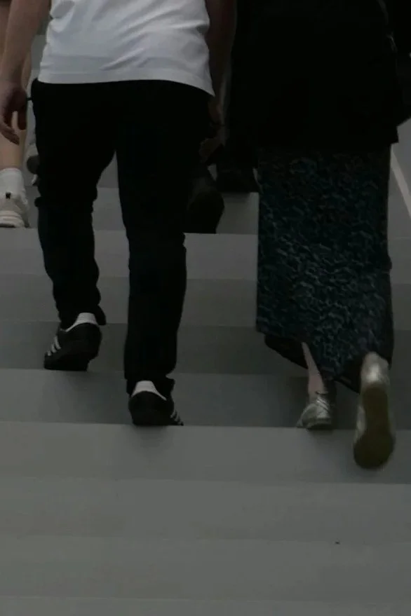 People walking up a set of light-colored stairs, only their lower bodies and feet visible.