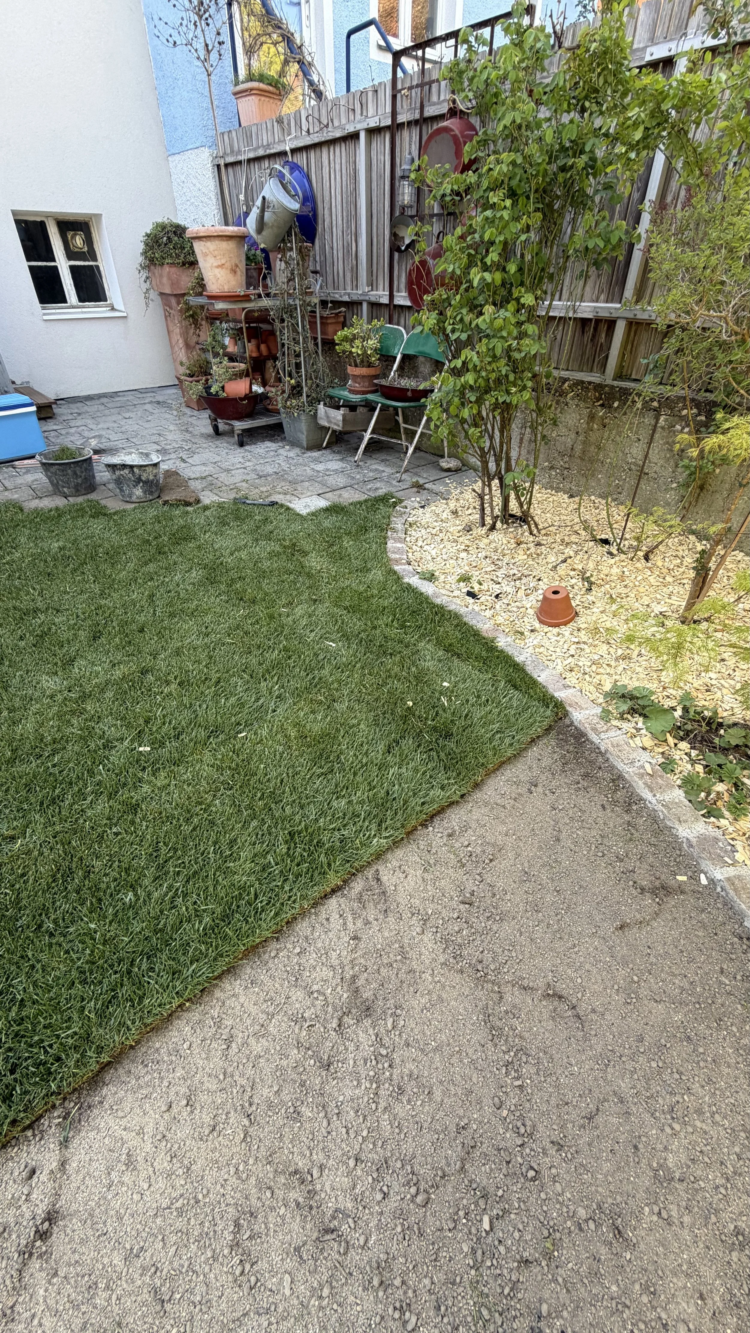 Garten mit grünem Rasen, Pflanztöpfen und Gartenmöbeln, umgeben von einem Holzzaun.