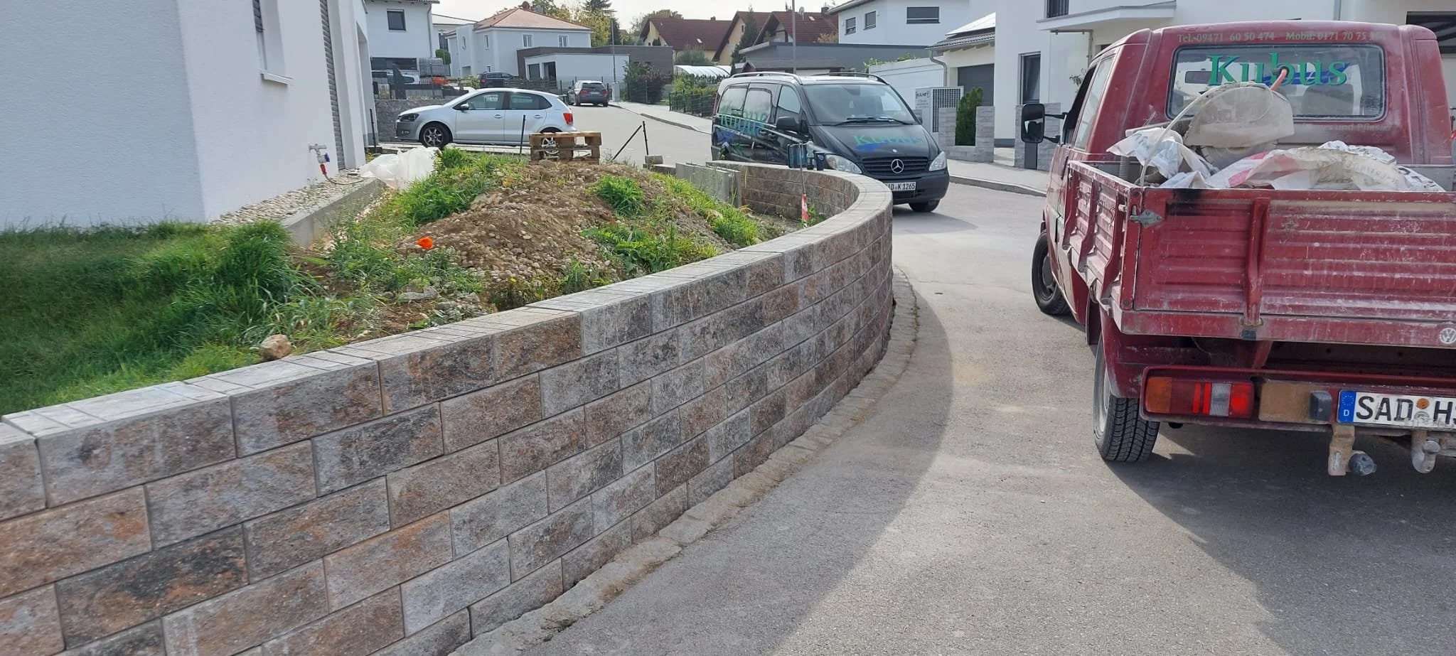 Kalthalle mit einigen Autos, einer Mauer, einem Garten und einem kleinen roten LKW auf einer Straße.