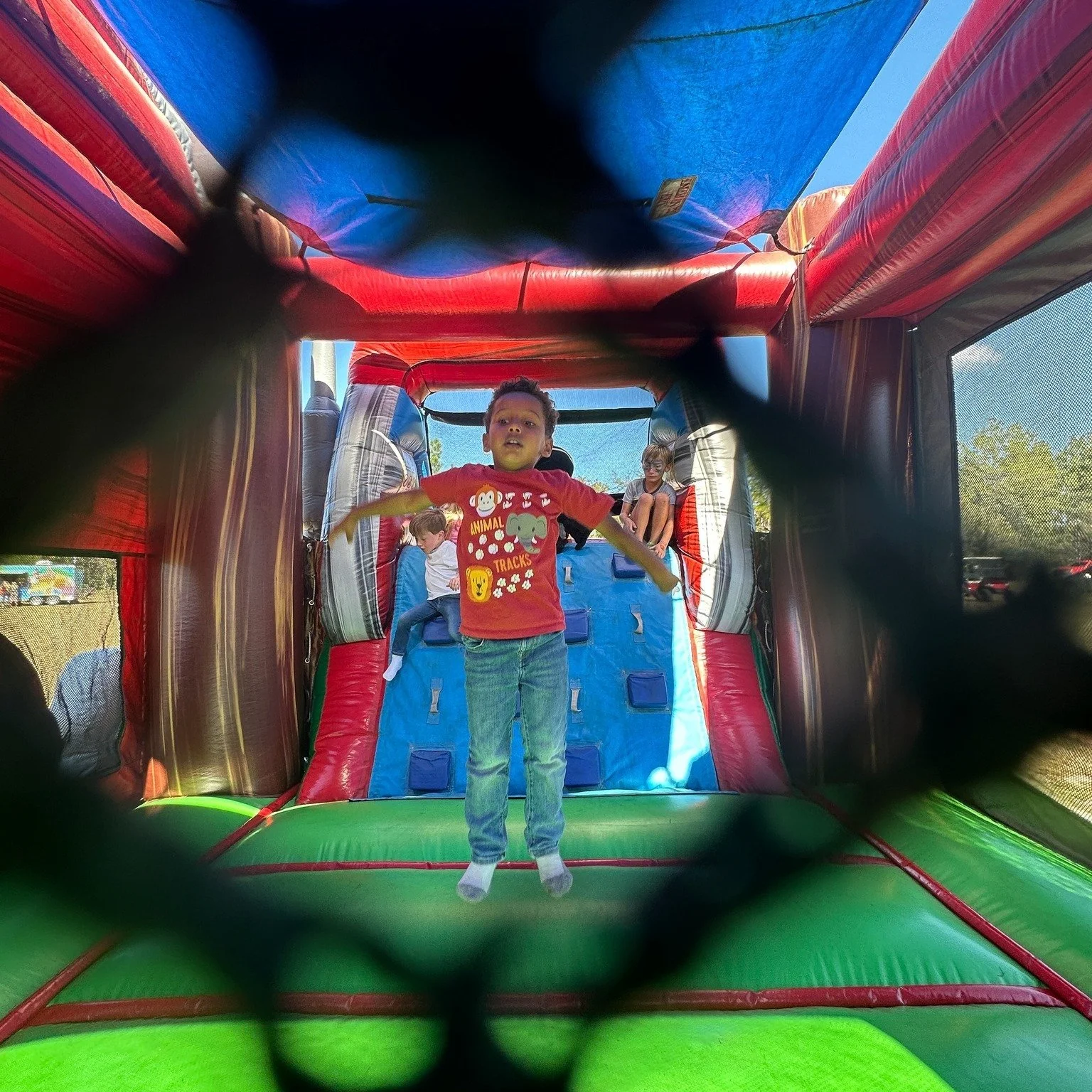 Children playing inside a colorful bounce house during daytime, viewed through a black safety net.
