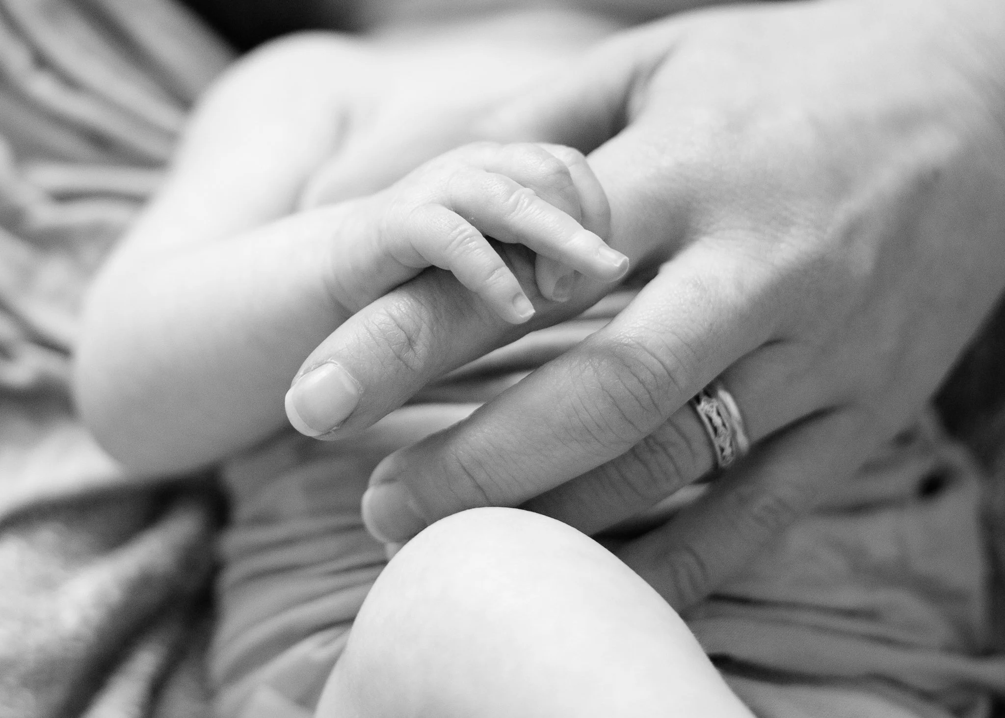 A close-up black and white photograph of a baby's hand grasping an adult's finger.