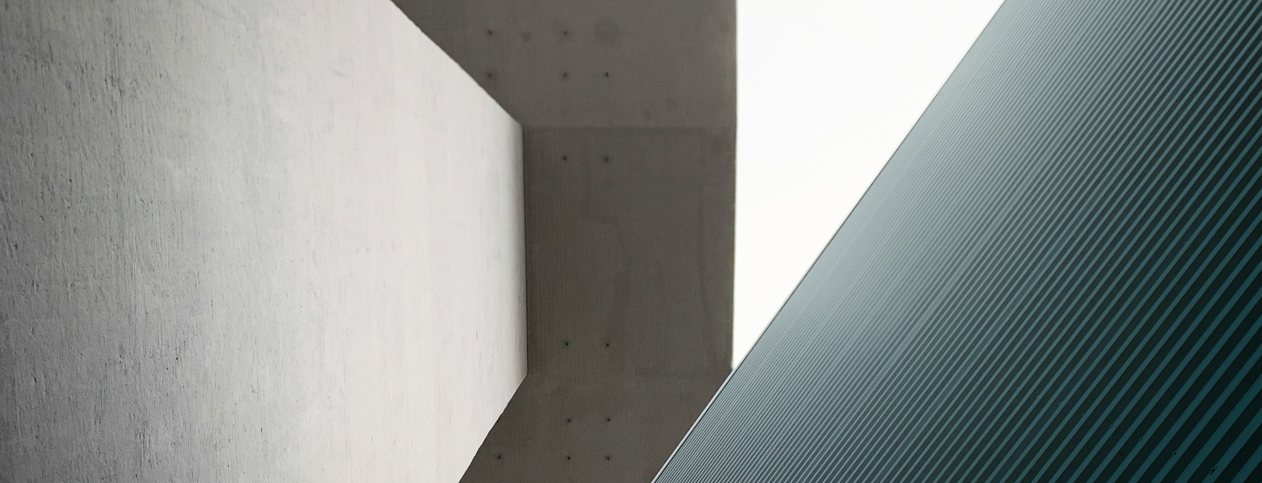 Ein architektonisches Detail eines Gebäudes mit einer weißen Wand und einer dunklen Decke, kombiniert mit einer diagonalen grauen und gestreiften Oberfläche.