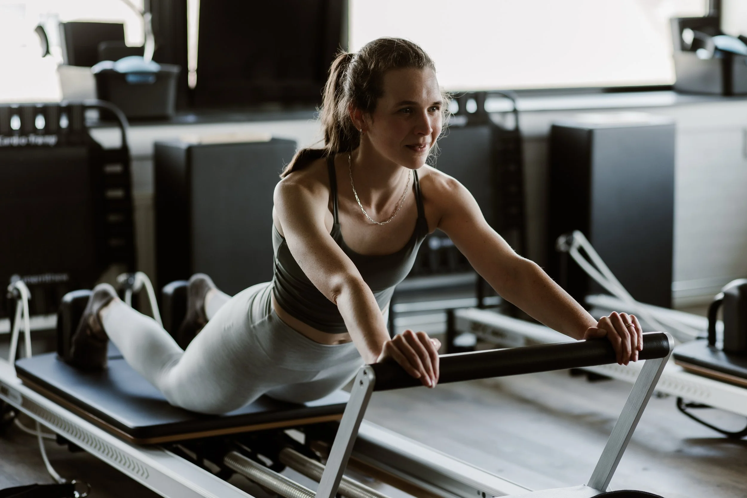 Vrouw doet fitnessoefening op een fitnessapparaat in een sportschool, met een achtergrond van sportschooluitrusting.