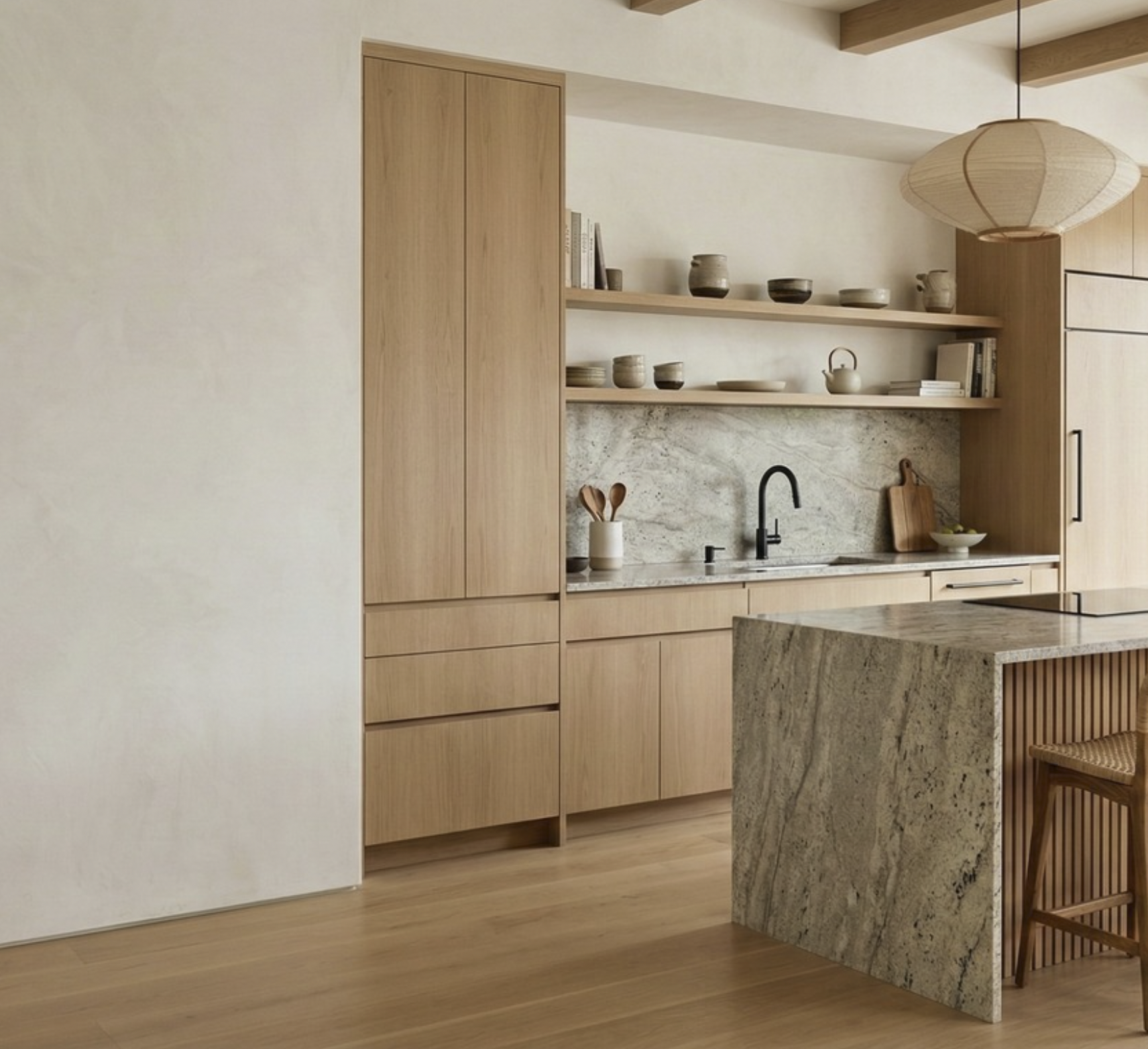 Cocina moderna con gabinetes de madera clara, estantes abiertos con vajilla, un fregadero negro, una isla de granito gris, y una lámpara de papel colgante.