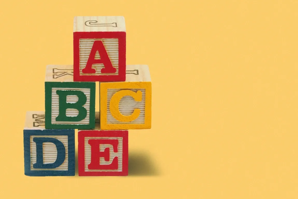 Colorful children's alphabet blocks spelling 'ABCDE' on a yellow background.