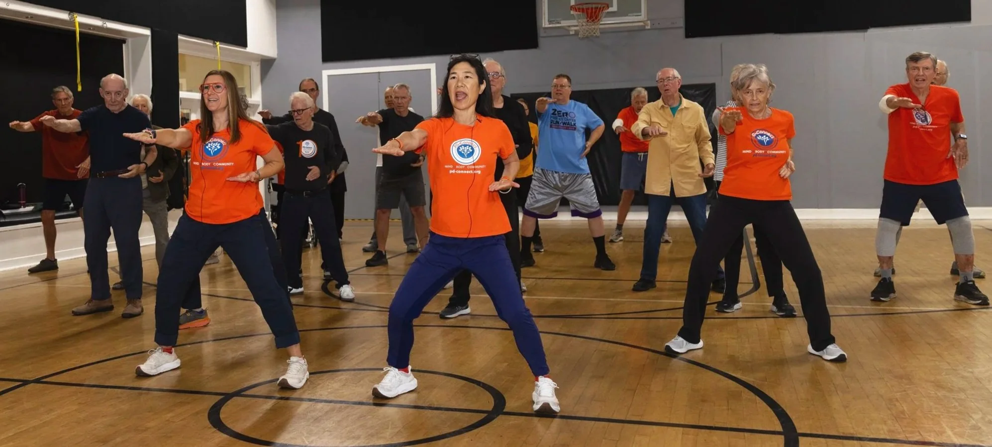 A group of older adults participating in a dance class in a gymnasium.