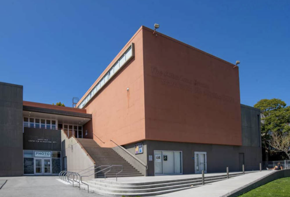Exterior view of a modern building with staircases, glass entrance doors, and a large, blank, reddish-brown wall.