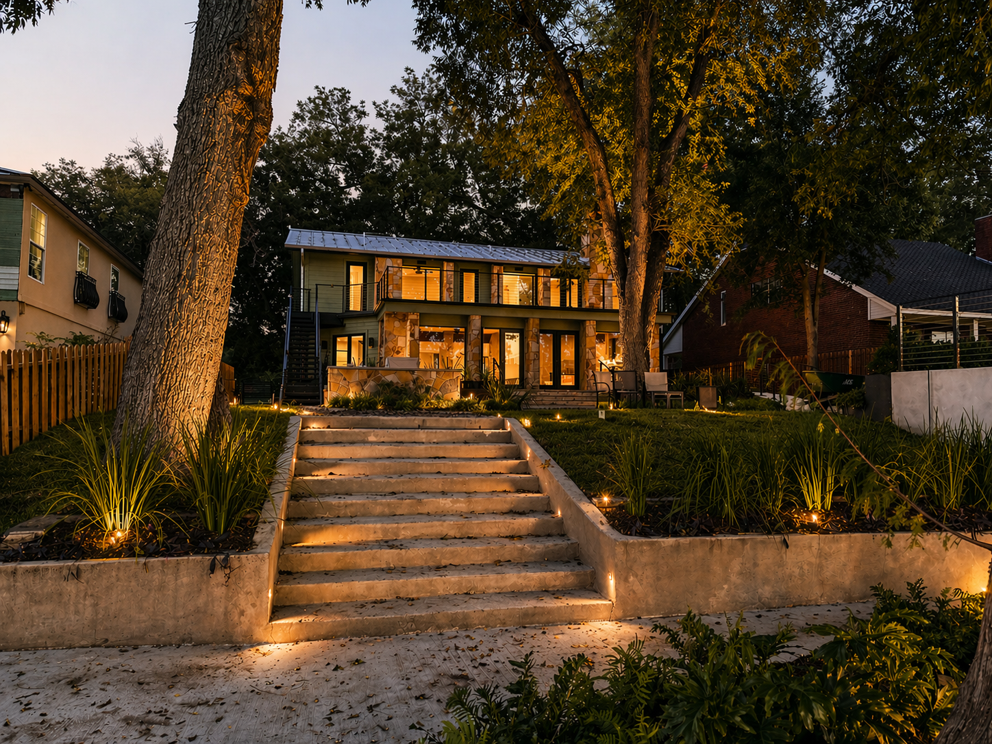 Back exterior of the Lake McQueeney Residence showing updated siding, standing seam metal roofing, shaded outdoor living areas, and the renovated home’s connection to the lakefront landscape.