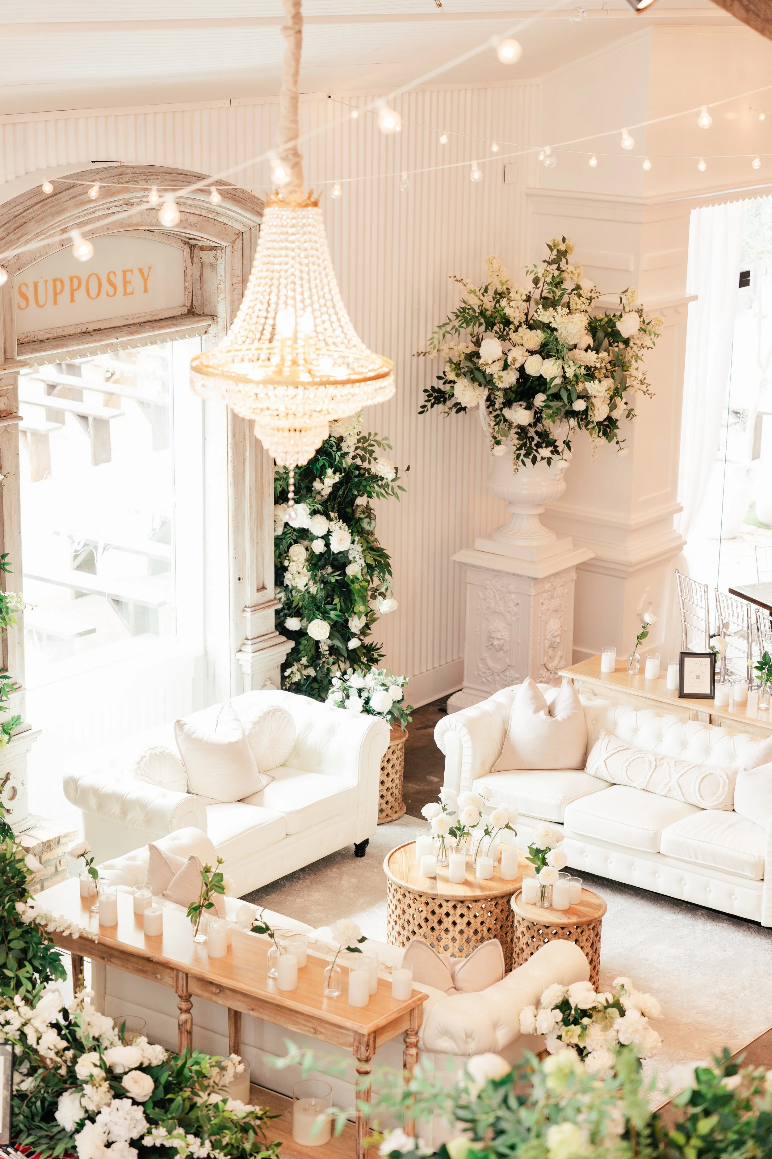 Elegant reception area with white sofas, floral arrangements, candles, and a chandelier.