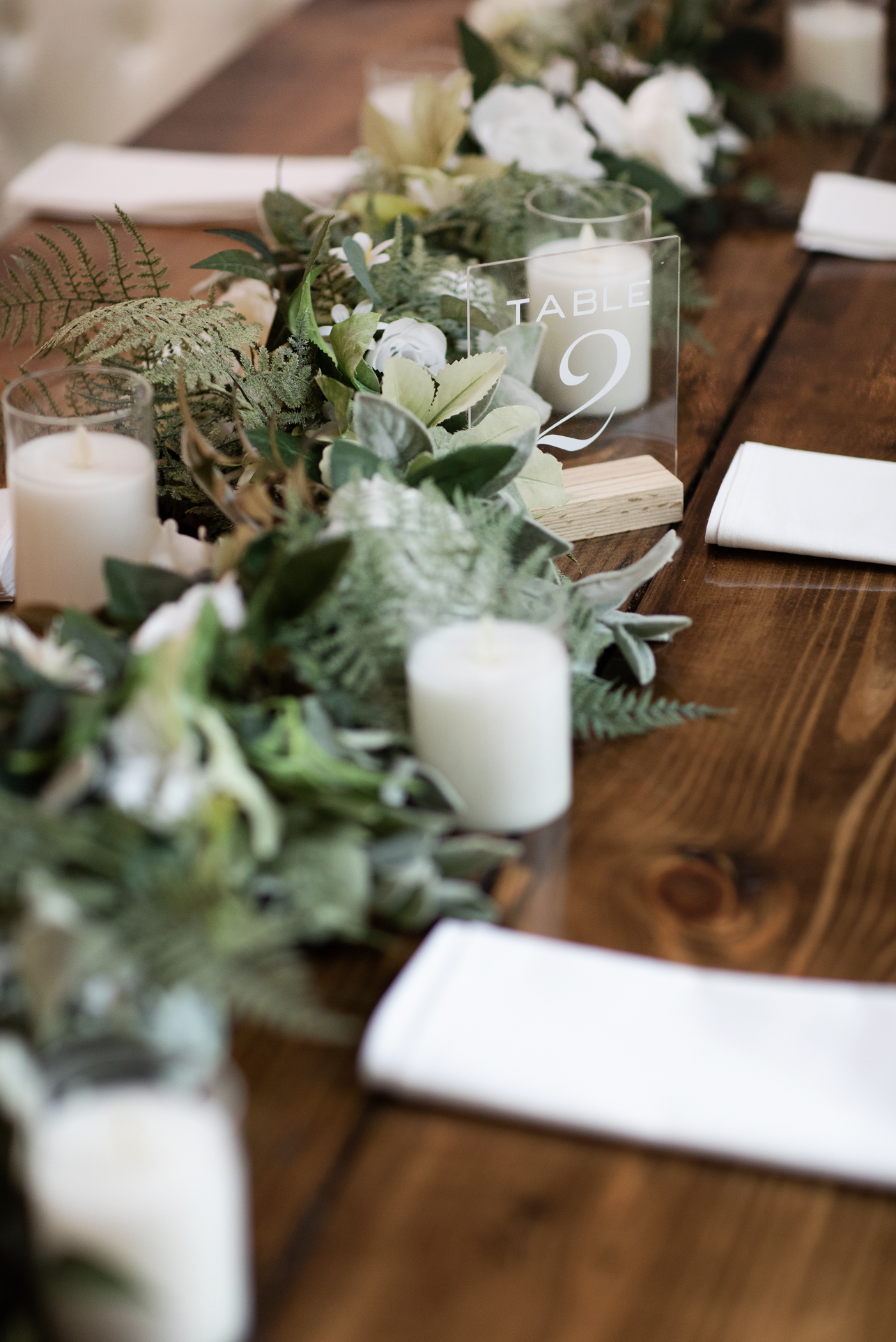 Wedding reception table with white candles, greenery centerpiece, and a table number sign in a Pensacola Wedding Venue.