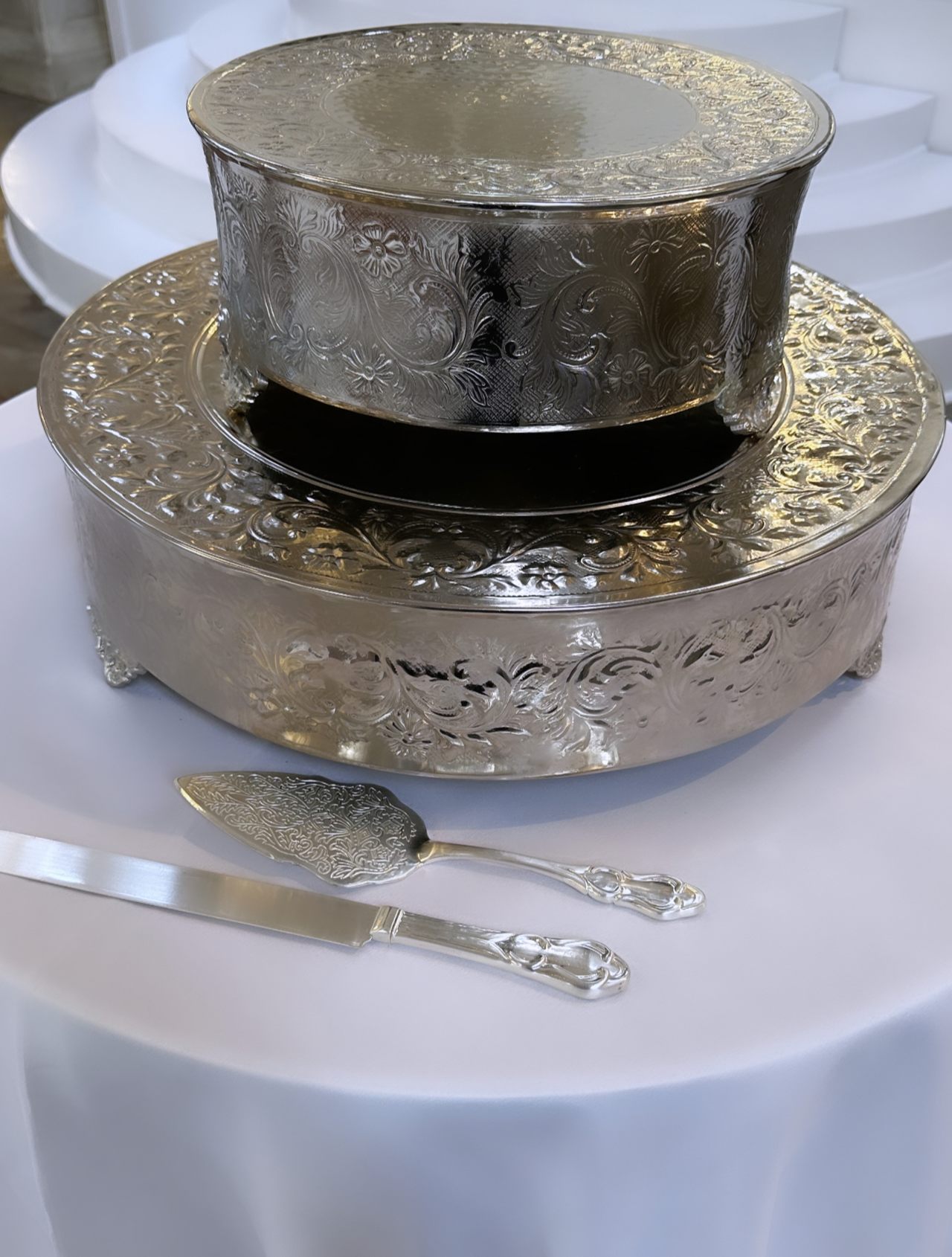 Decorative silver serving containers on a white tablecloth with a cake knife and server.