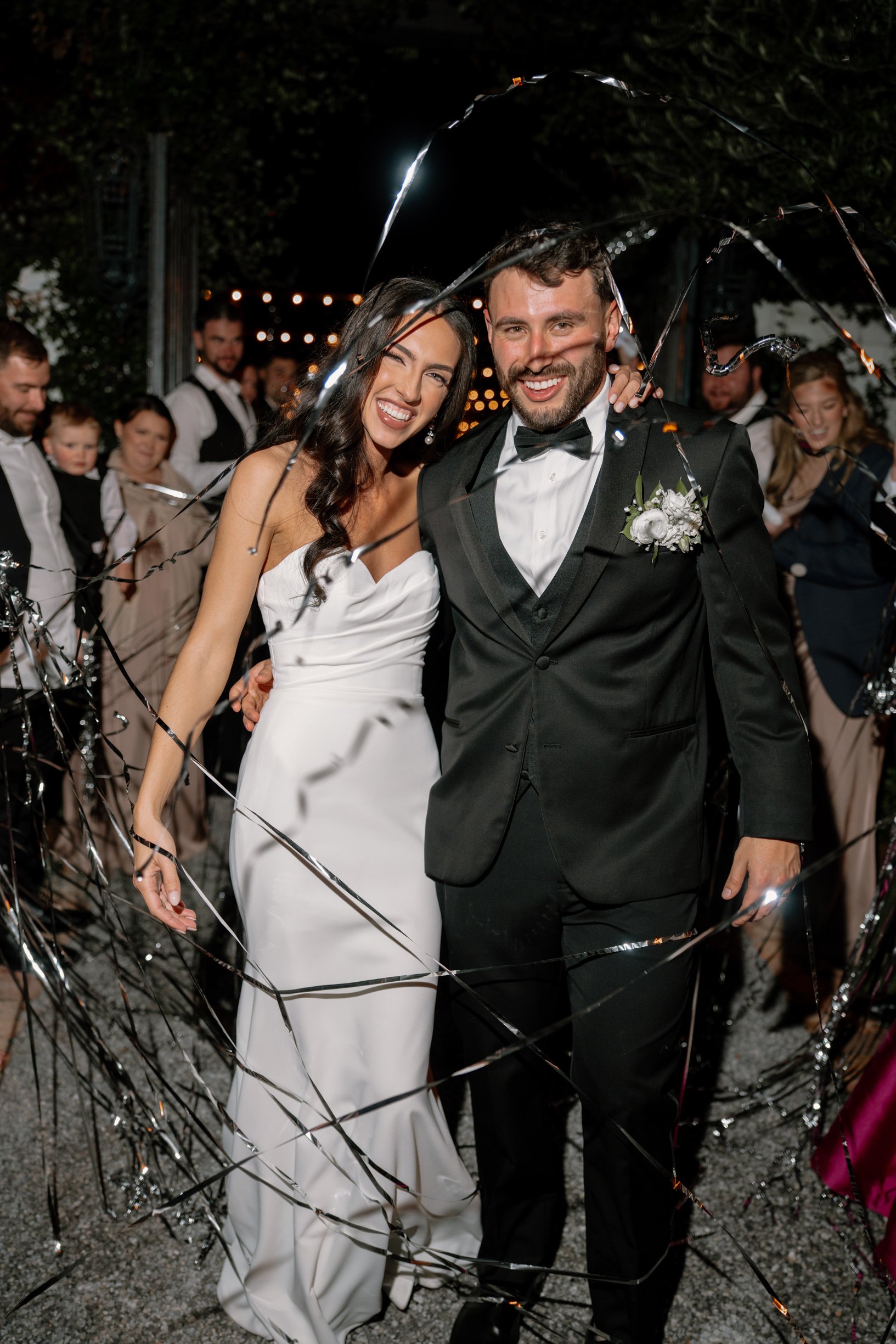 Bride and groom smiling under an umbrella during their wedding celebration, surrounded by friends and family in Pensacola, Florida.