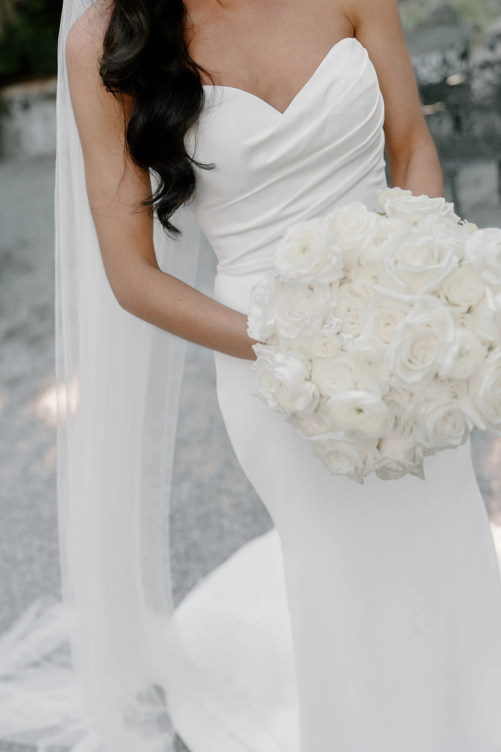 A bride in a white wedding dress holding a large bouquet of white roses.