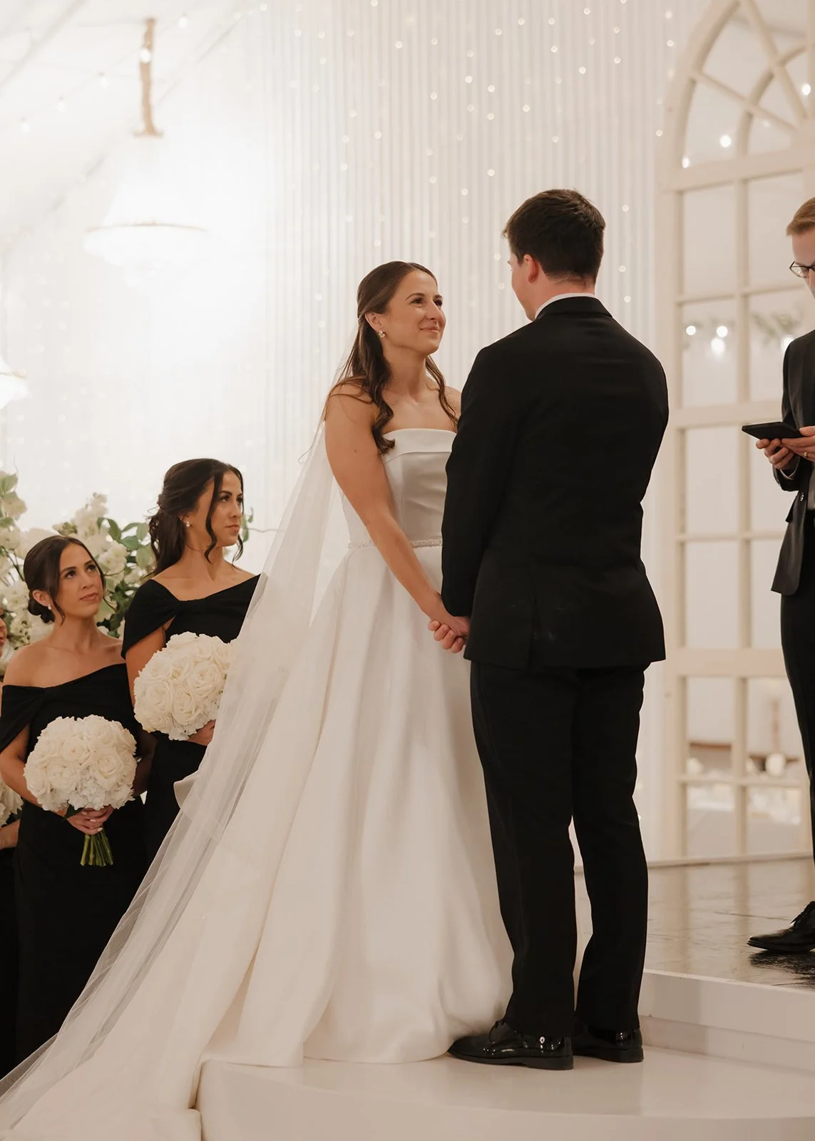 A couple getting married at their wedding ceremony, holding hands and exchanging vows, with bridesmaids holding bouquets in the background in a Pensacola Wedding Venue.