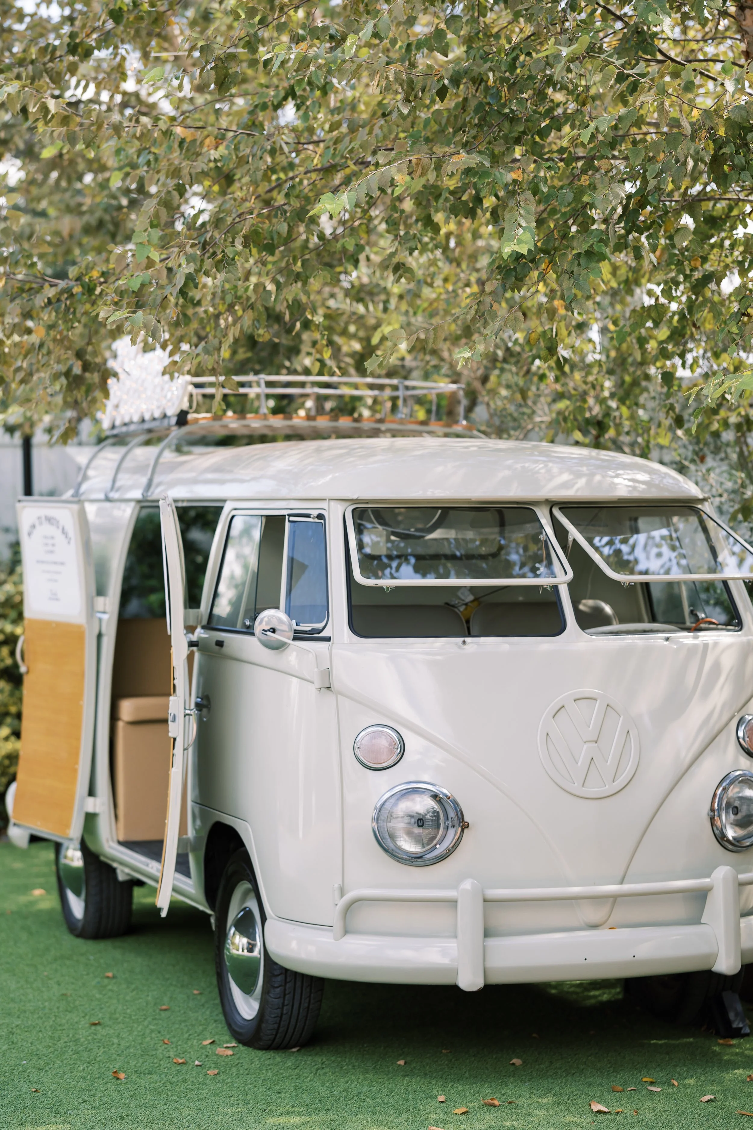 A white vintage Volkswagen camper van parked on green grass with trees in the background of a Pensacola Wedding Venue.