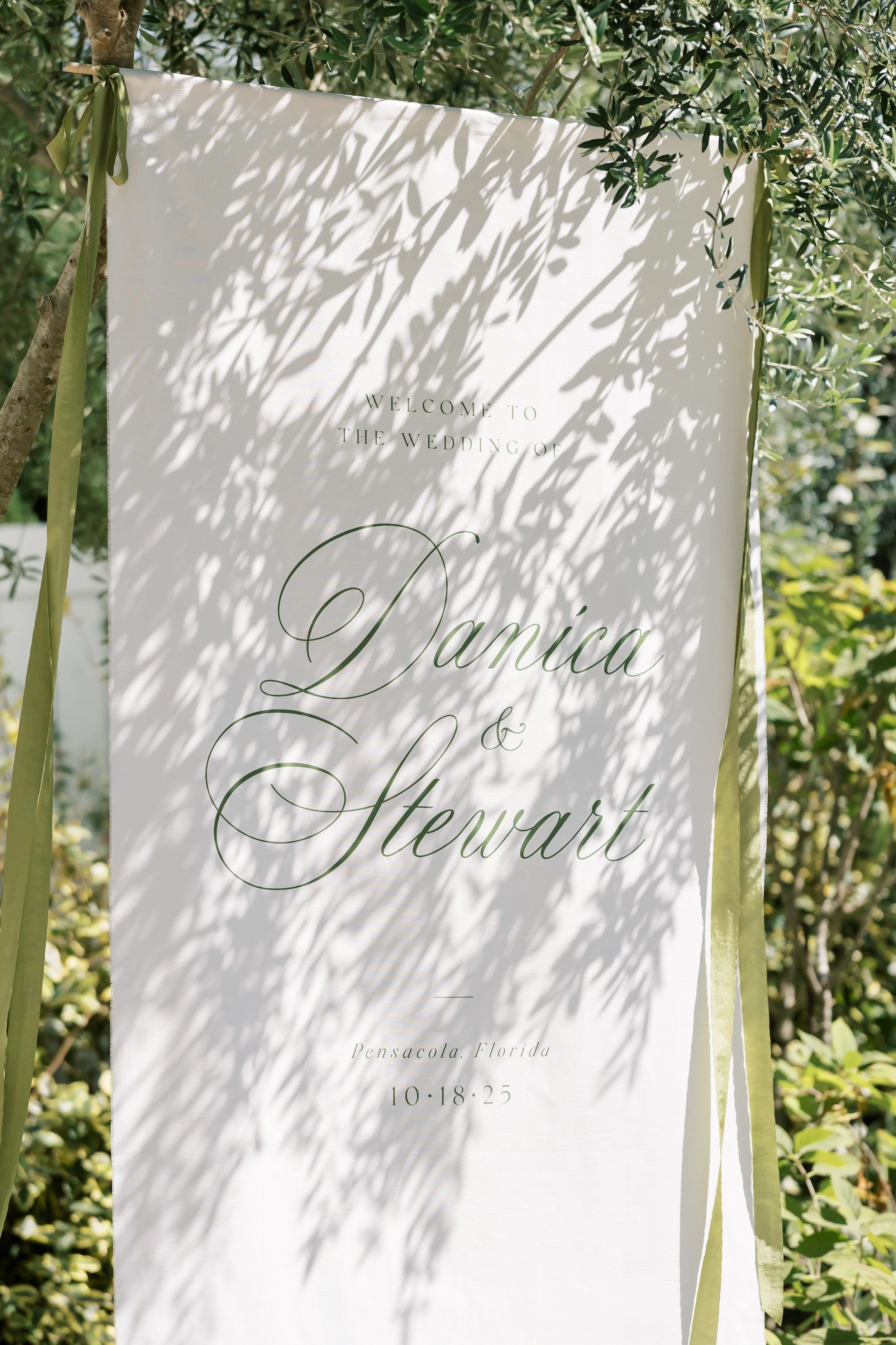 Wedding welcome sign with shadows of leaves, displaying the names 'Danica & Stewart' and the date '10.18.25' in Pensacola, Florida.