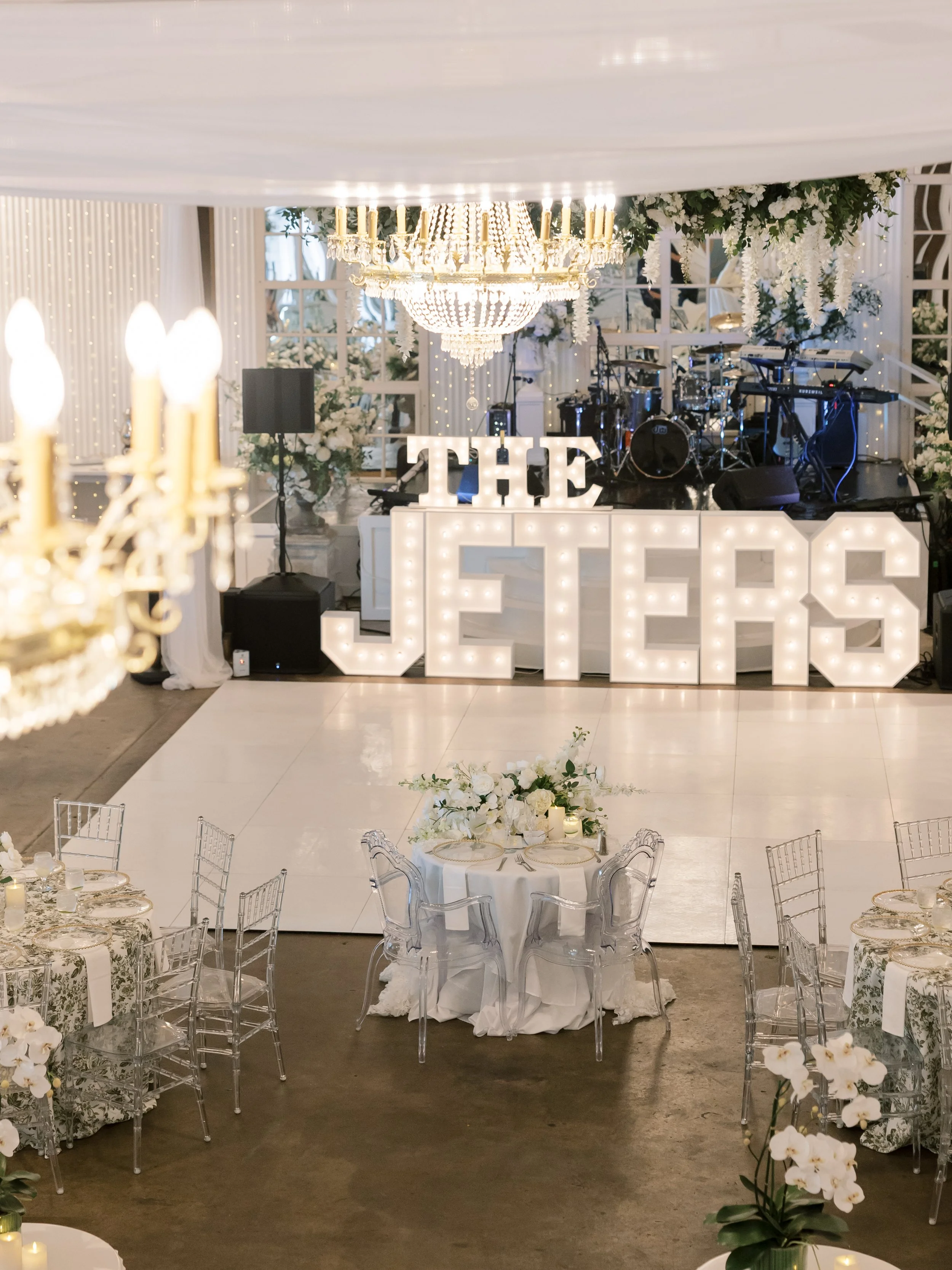Wedding reception with illuminated sign saying 'The Jets,' decorated with flowers, chandeliers, and a stage with musical instruments.