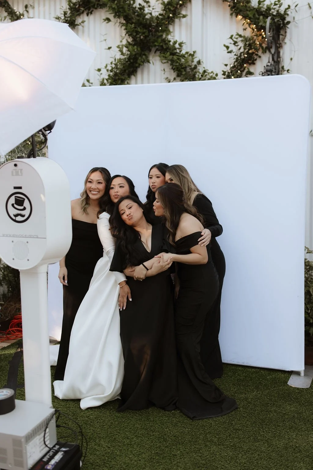 Group of six women dressed in elegant black and white outfits posing for a photo in front of a white backdrop at an outdoor Pensacola Wedding Venue.