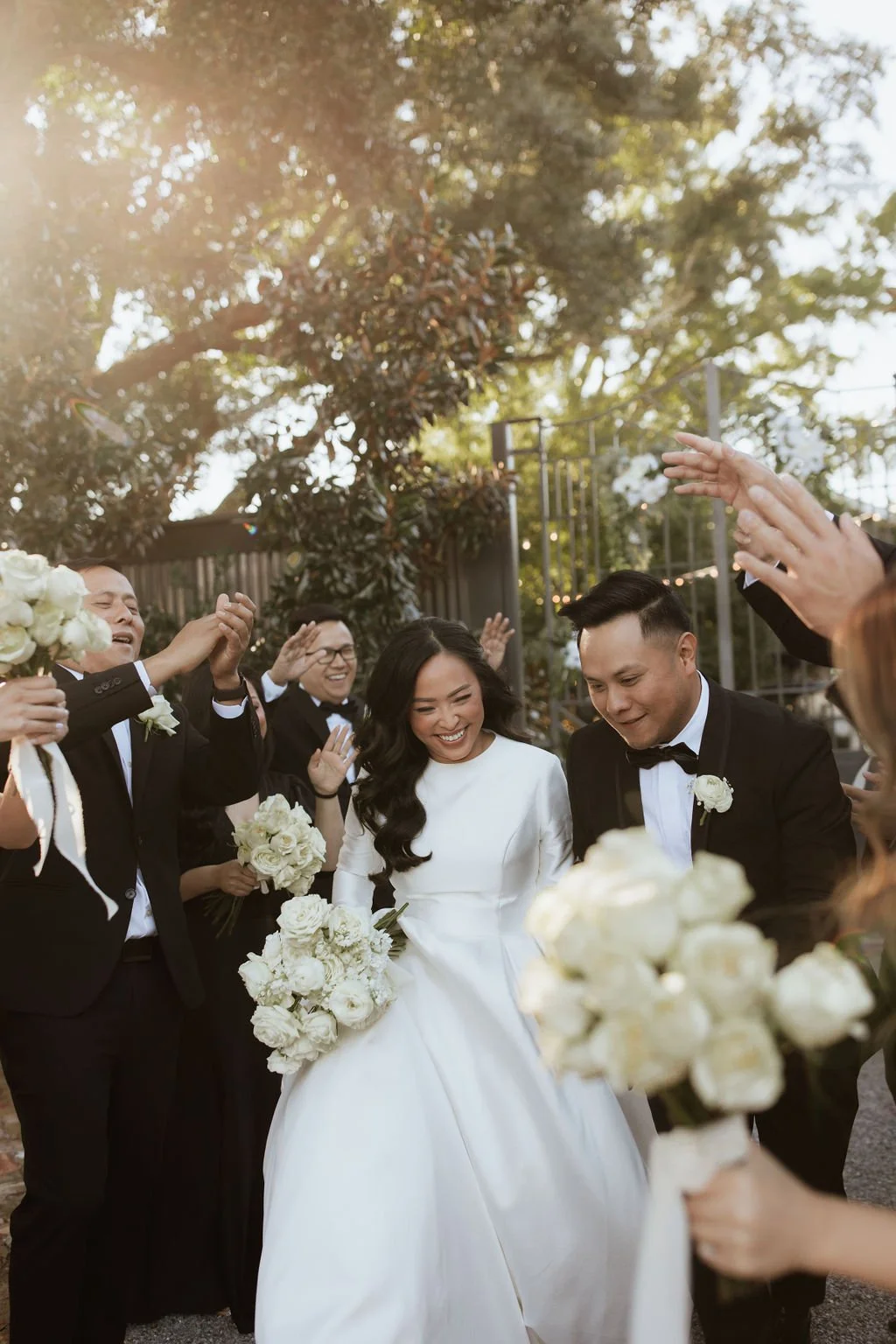 Bride and groom celebrating with friends at wedding, surrounded by people in formal attire and holding white bouquets outdoors in Pensacola, Florida