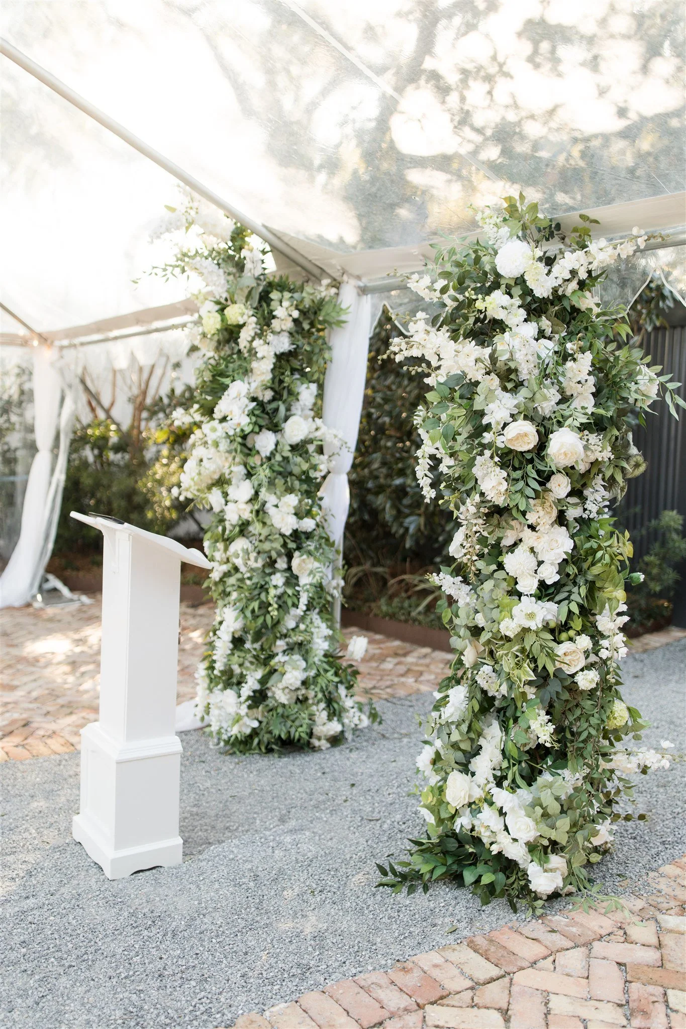 White floral arch and pedestals at a wedding ceremony outdoors.