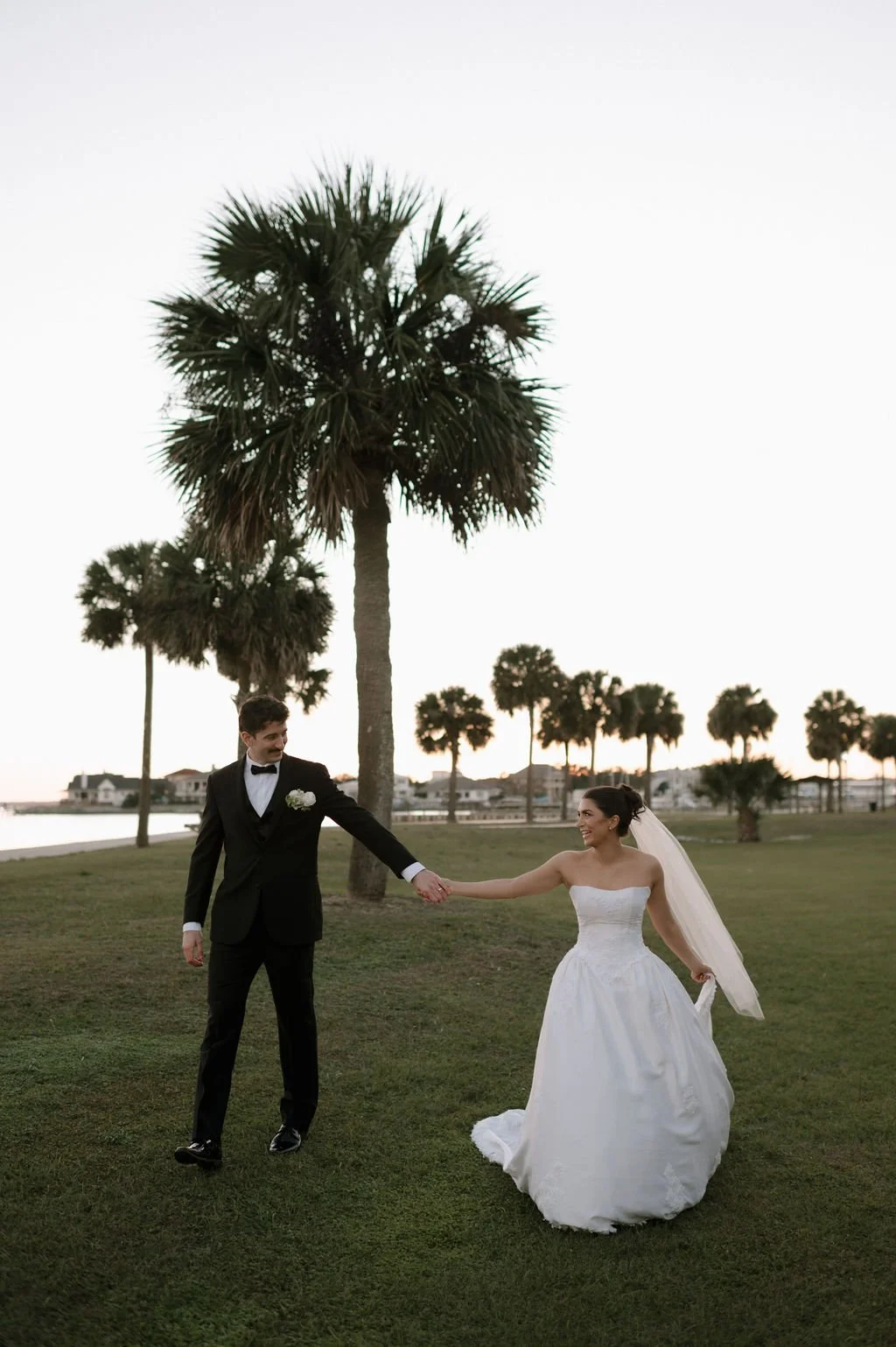 A bride and groom holding hands and dancing in a park with palm trees during a pensacola sunset.