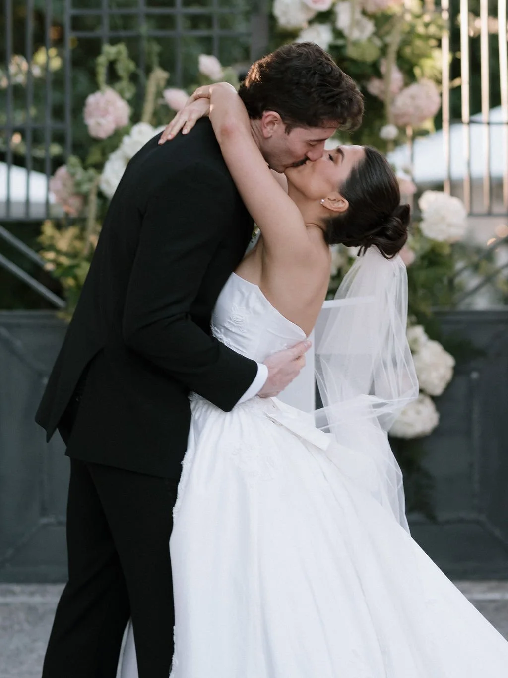 A bride and groom kissing at their Pensacola wedding ceremony, with flowers in the background.