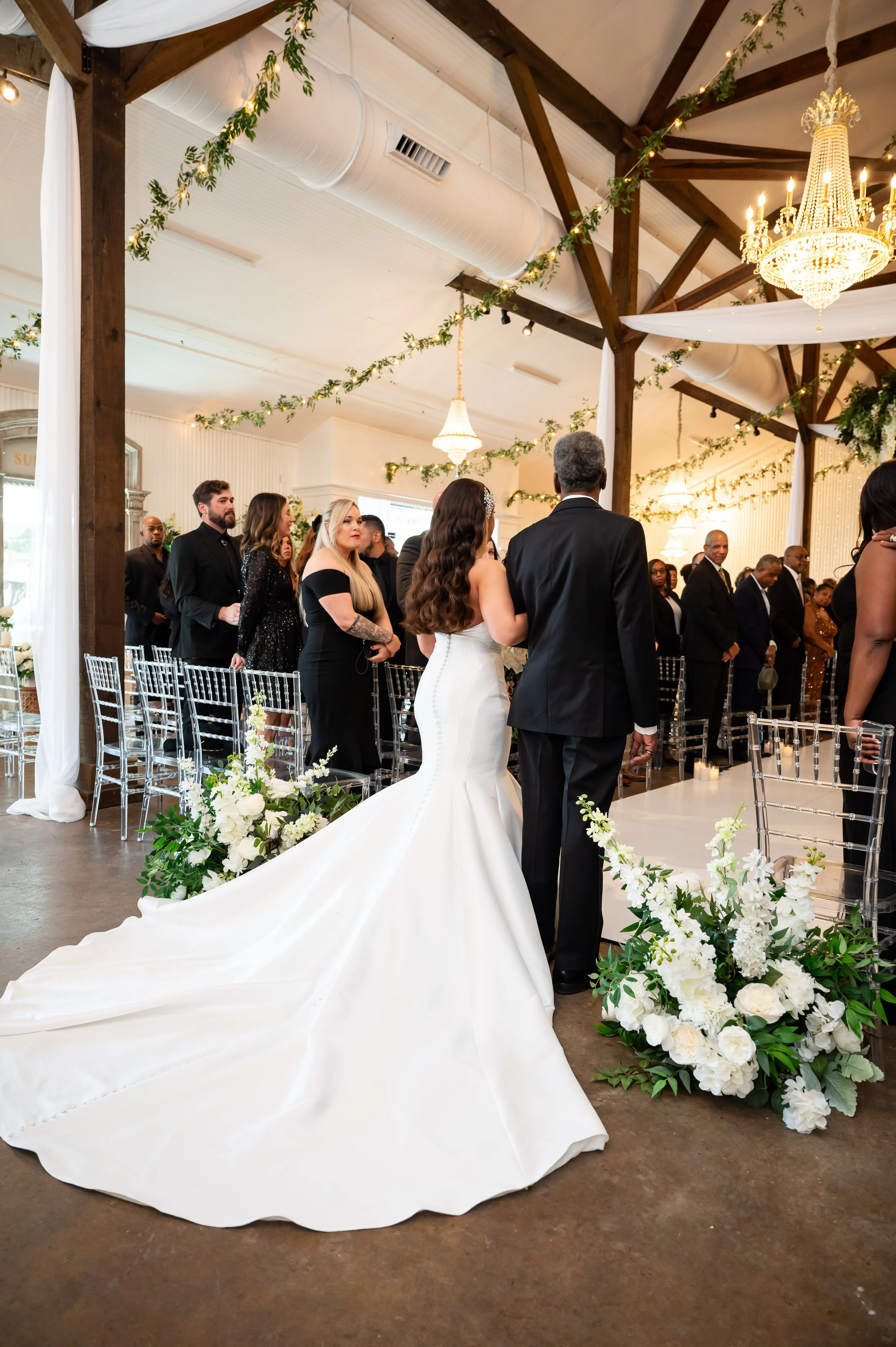 A bride in a white wedding gown walking down the aisle with her father at a wedding ceremony in an elegant decorated Pensacola Wedding Venue.
