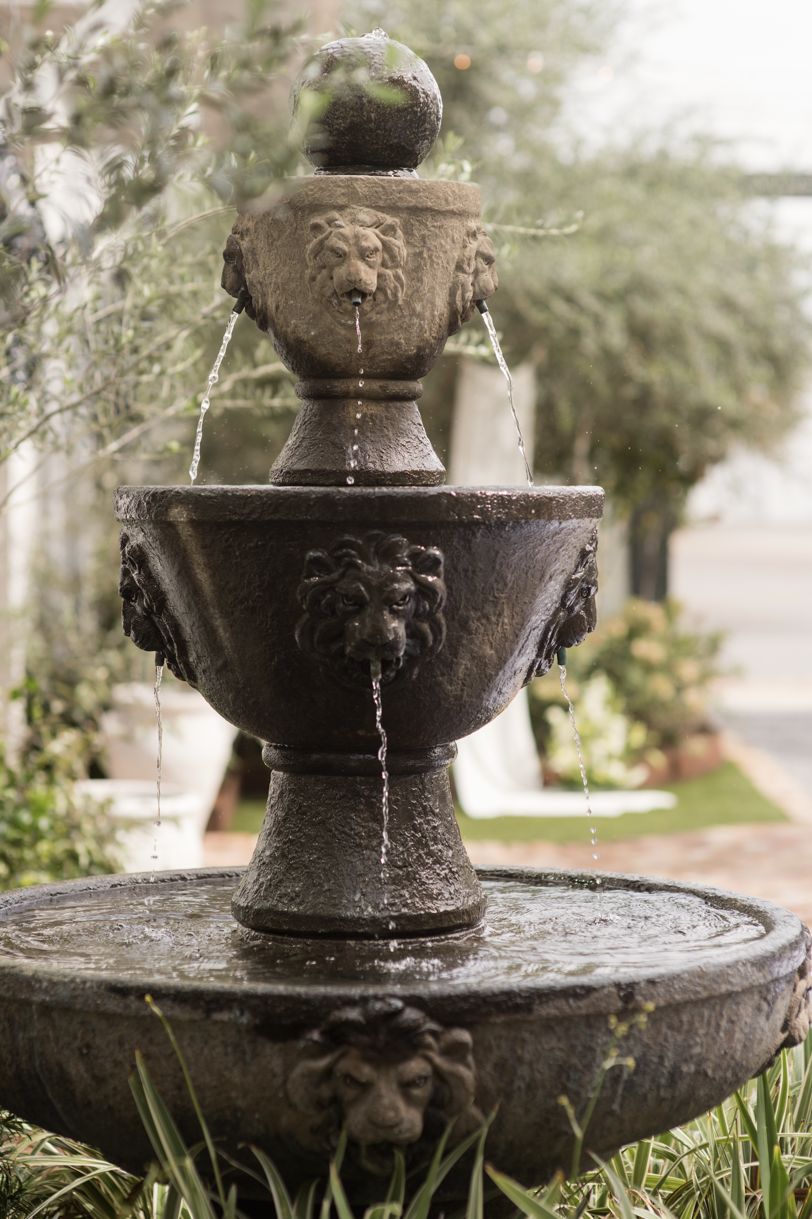 Three-tier outdoor fountain with lion head sculptures from which water flows.