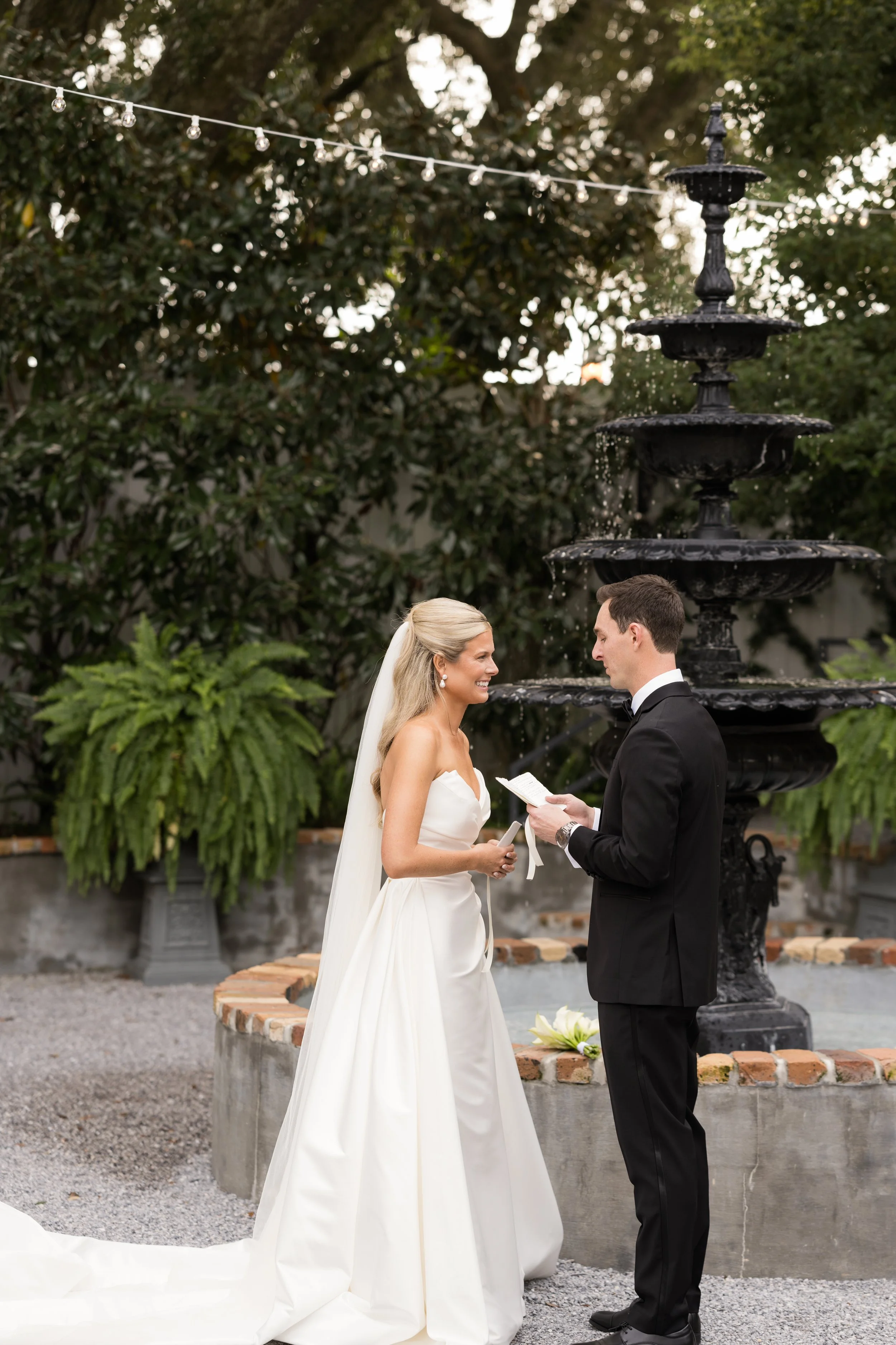 A bride and groom exchanging vows in front of a black fountain during a wedding ceremony outdoors at a Pensacola Wedding Venue.