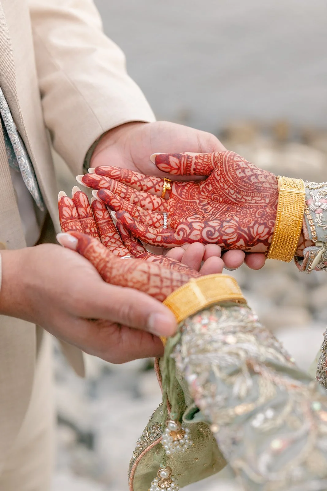Close-up of a groom holding hands with a bride during a wedding ceremony, with a focus on their hands and intricate henna designs on the bride's hands.