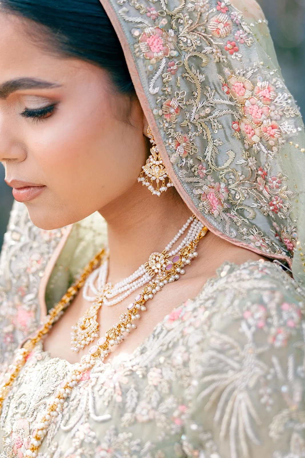 Close-up of a woman dressed in traditional, ornate wedding attire with intricate embroidery, gold jewelry, and a pastel-colored embroidered dupatta.