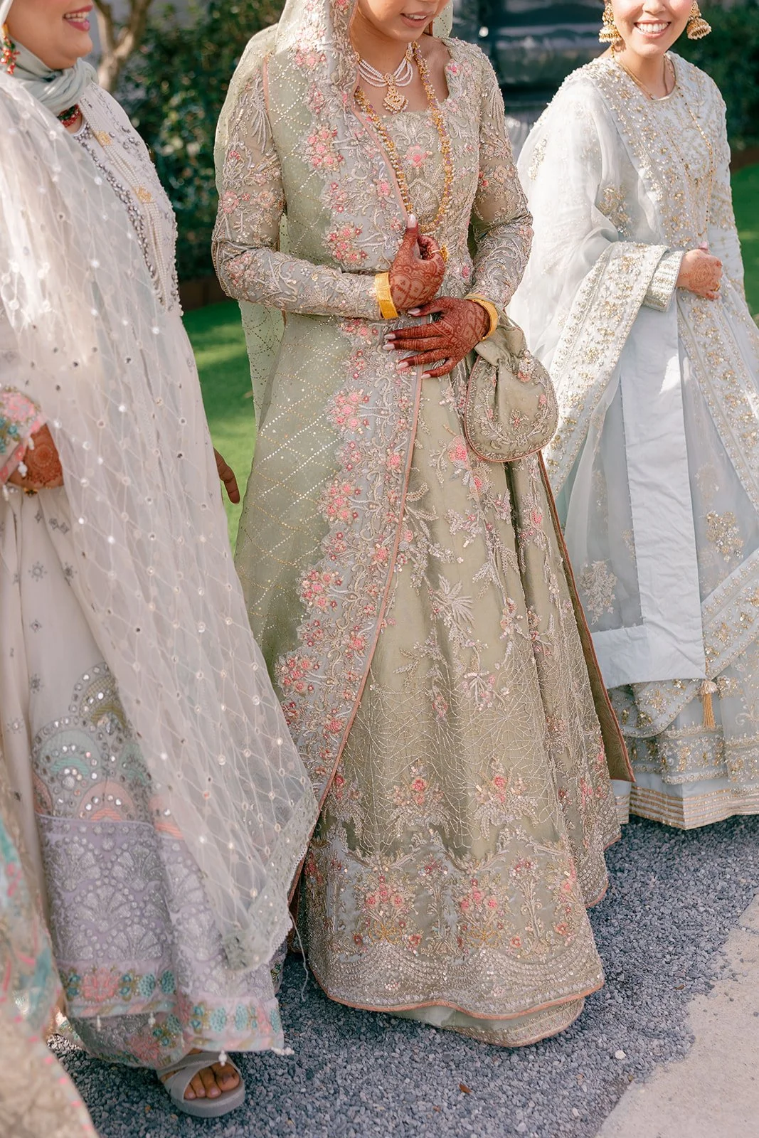 Women dressed in traditional South Asian wedding attire, with ornate embroidery and jewelry, standing outdoors.
