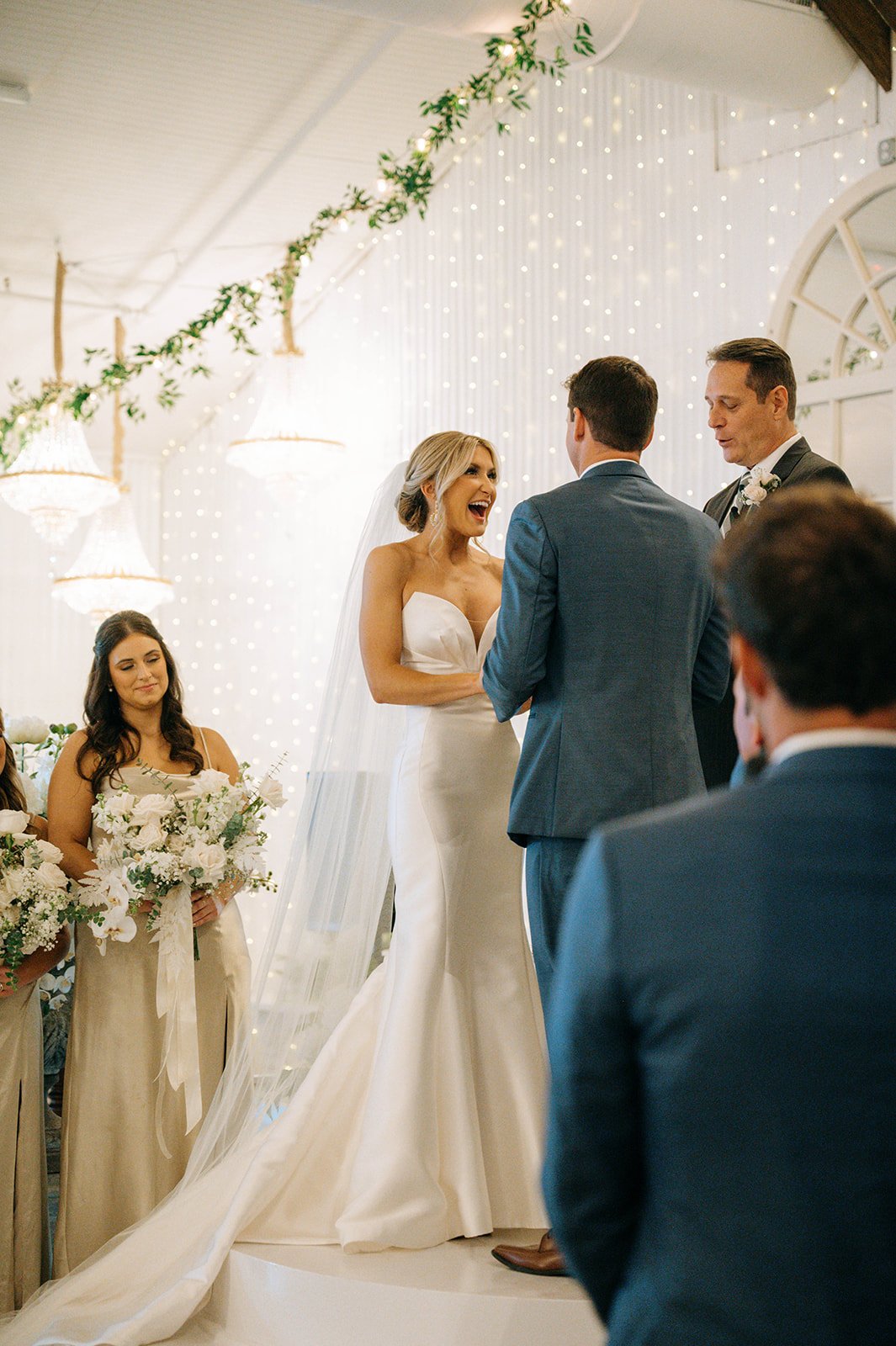 A Pensacola wedding ceremony with a bride and groom exchanging vows, surrounded by bridesmaids and groomsmen, decorated with string lights and greenery.