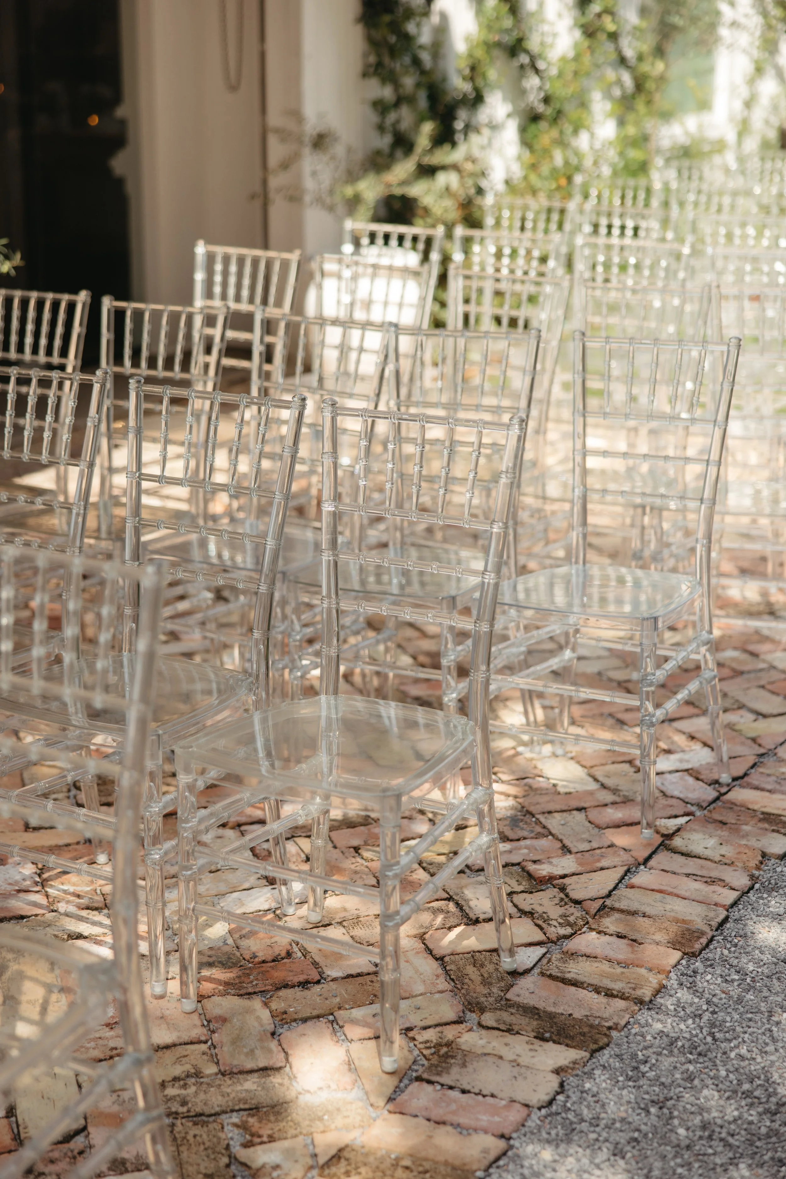 Empty transparent acrylic chairs arranged outdoors on a brick patio.