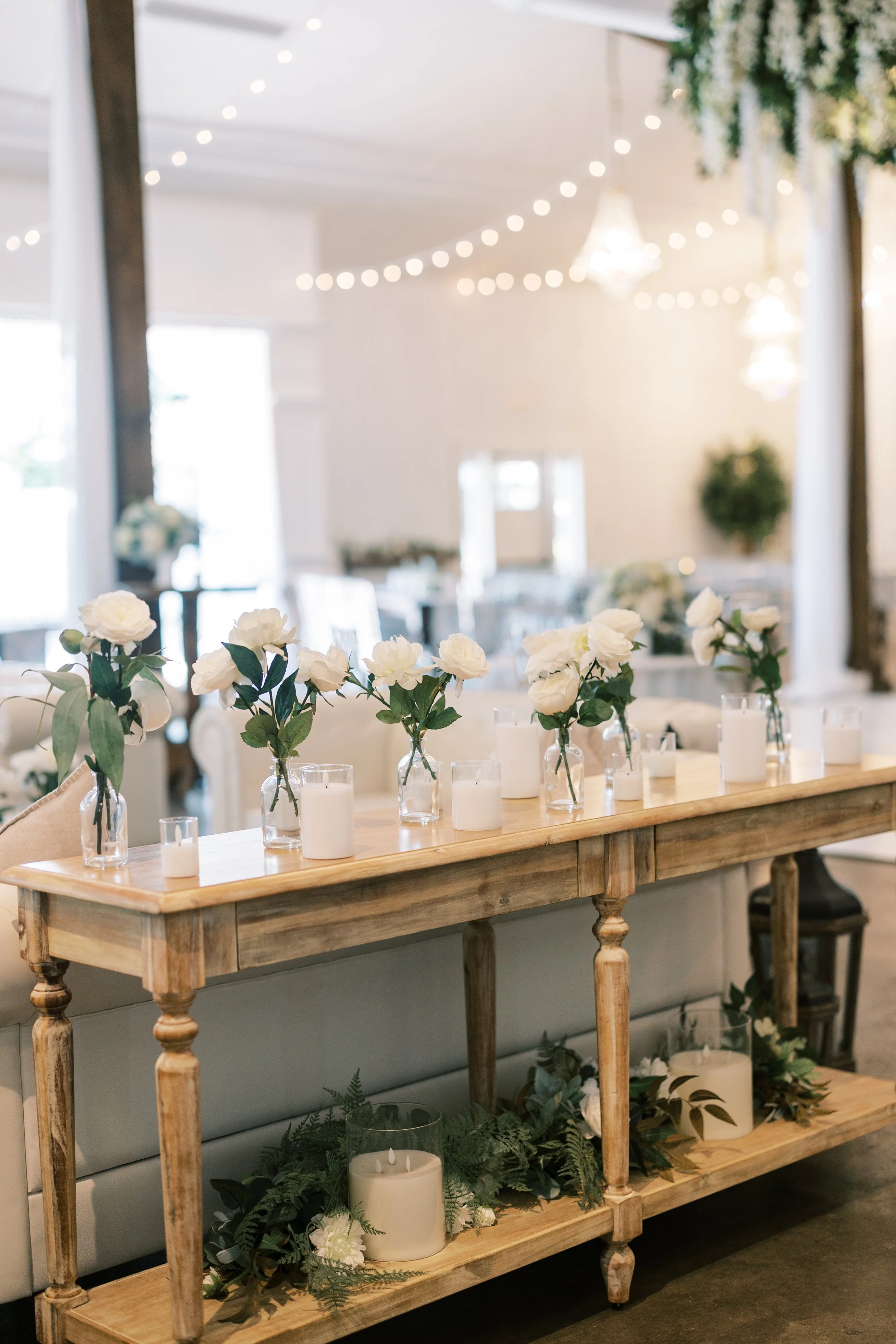 Elegant table decor with white flowers, candles, and greenery in a softly lit room, likely for a wedding or special event in a Pensacola Wedding Venue.